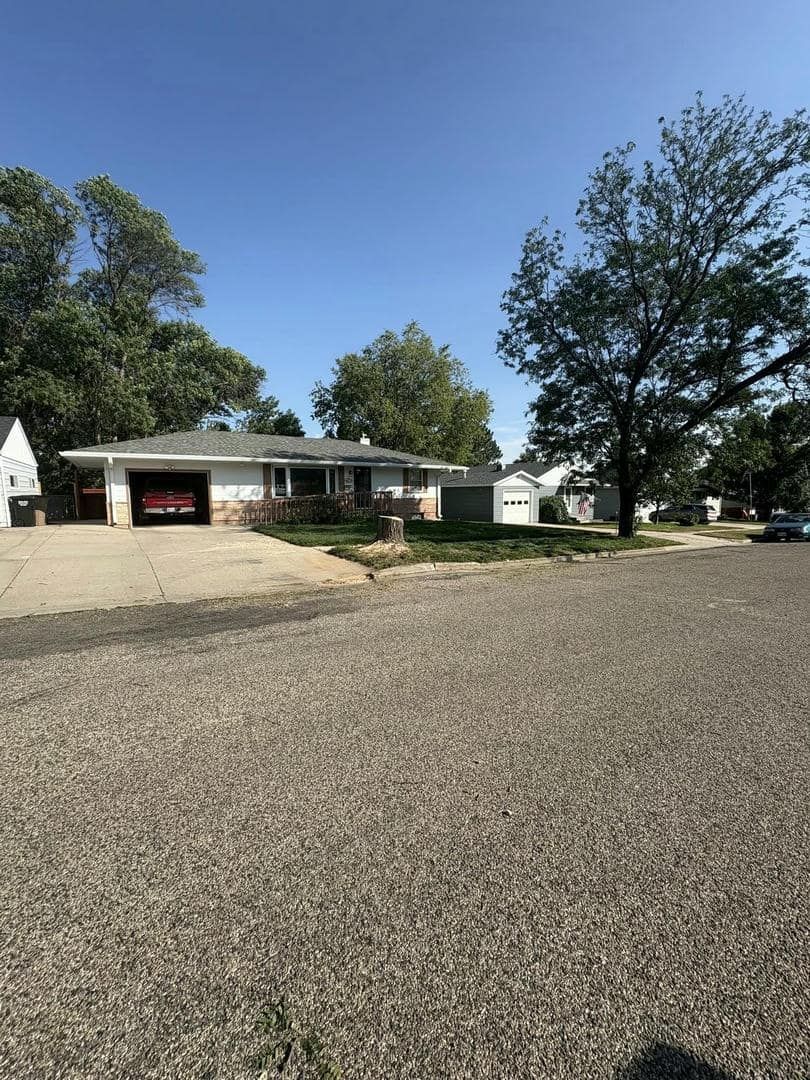 Single-story house with a gravel driveway and small yard on a sunny day. A red car is in the garage.
