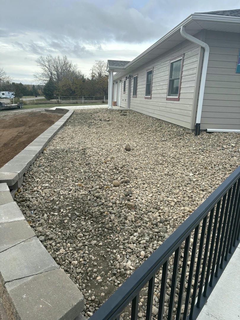 Exterior of a building with gravel landscaping, a retaining wall, and a black railing.