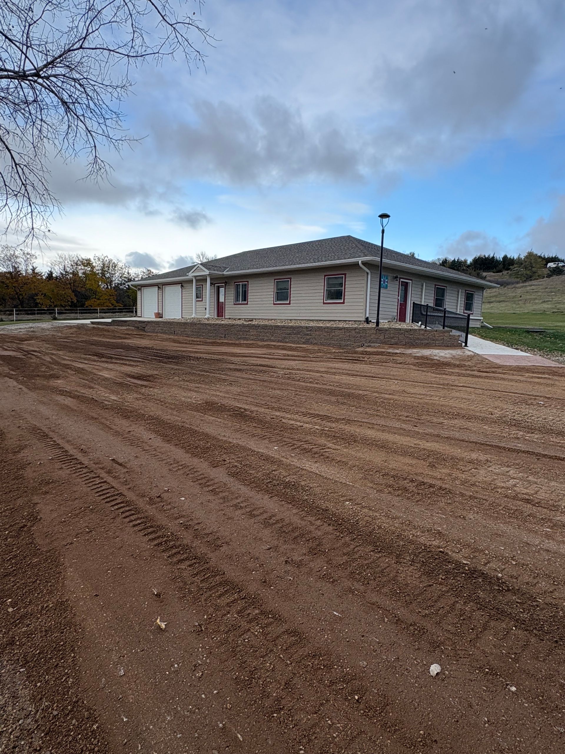 House with gravel yard, cloudy sky. Brown dirt, tire tracks, and siding visible.