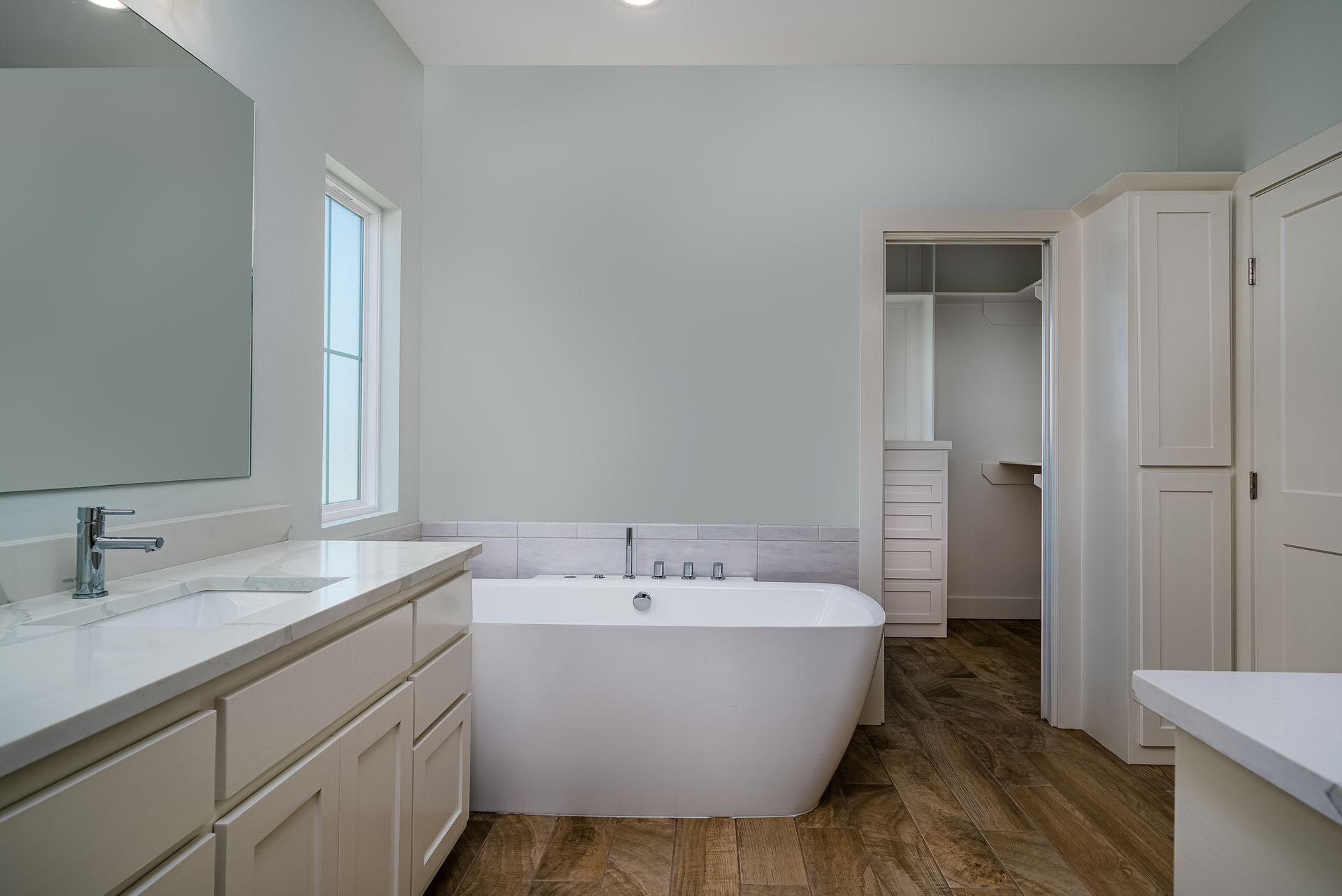 A bathroom with a bathtub , sink , mirror and walk in closet.