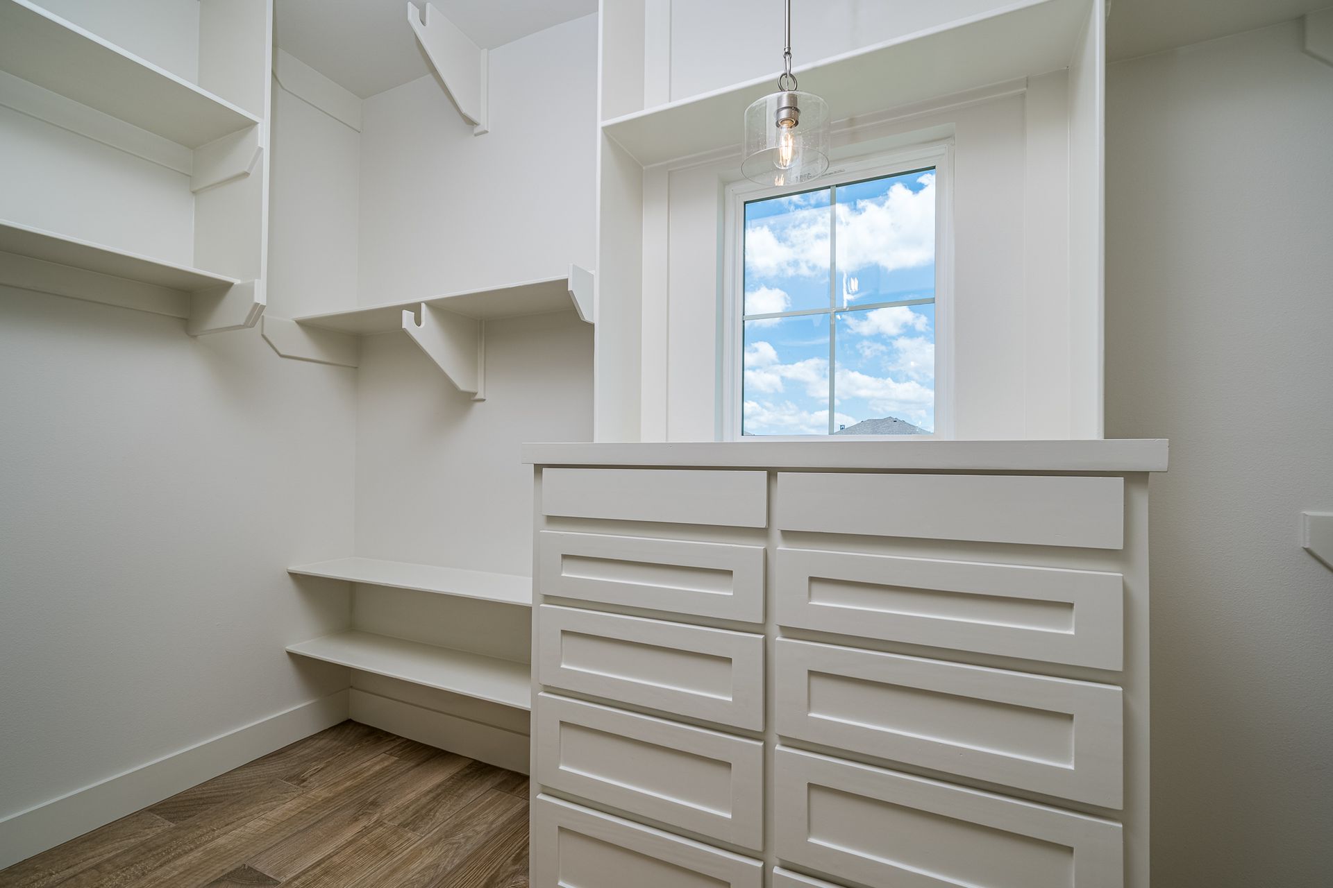 A walk in closet with lots of shelves and drawers and a window.