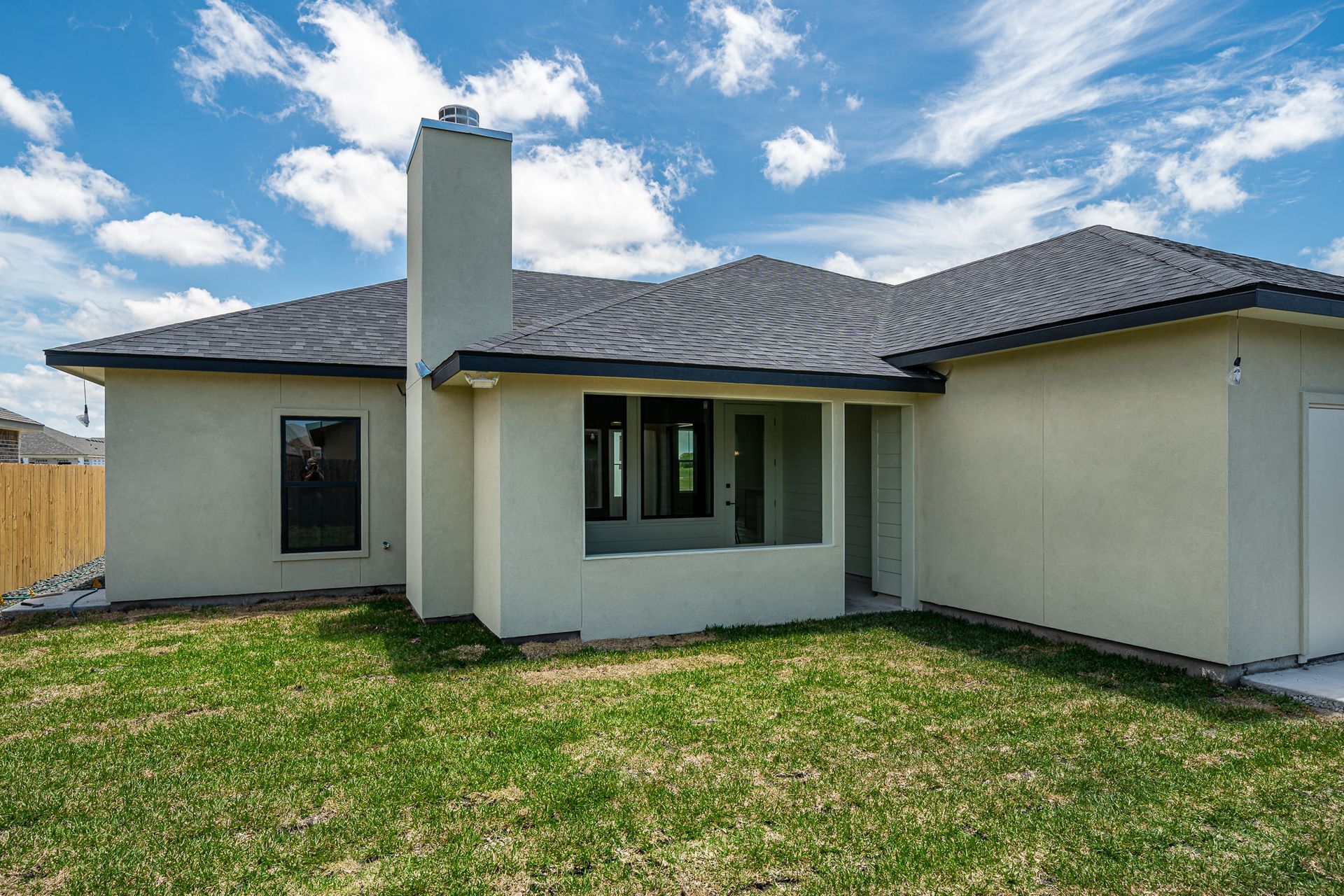 A white house with a gray roof and a chimney in the backyard.
