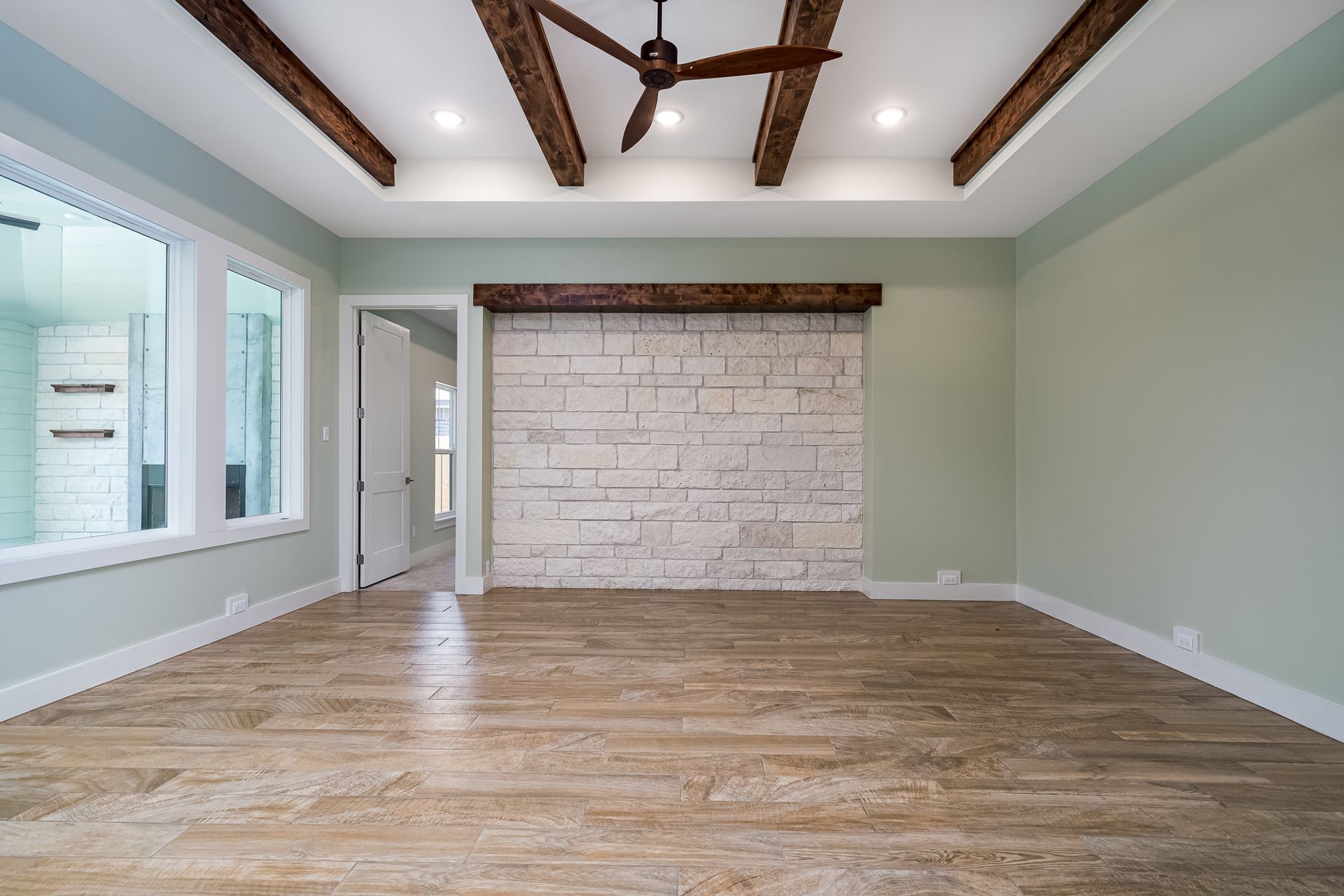 An empty living room with a brick wall and a ceiling fan.