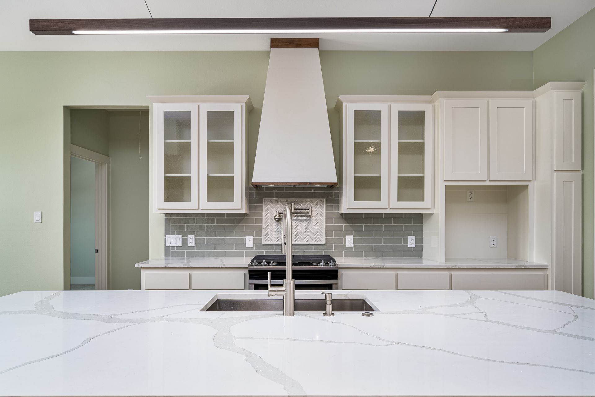 A kitchen with white cabinets , a stove , a sink , and a hood.