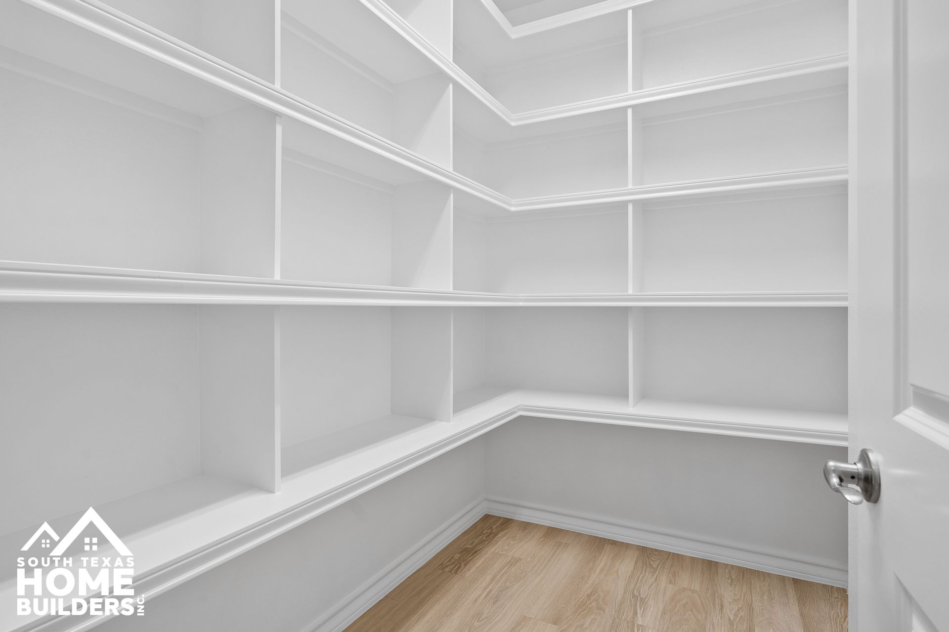 Empty white pantry with multiple shelves and wooden floor.