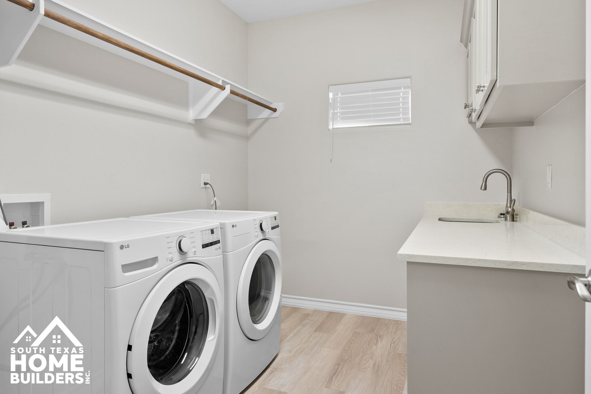 Laundry room with a washer, dryer, sink, cabinets, clothes rack, and window.