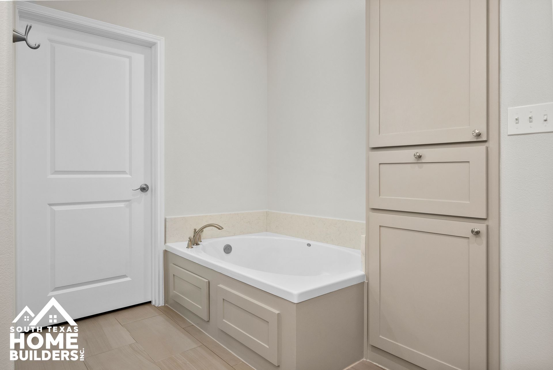 Bathroom with a white tub and beige cabinets.