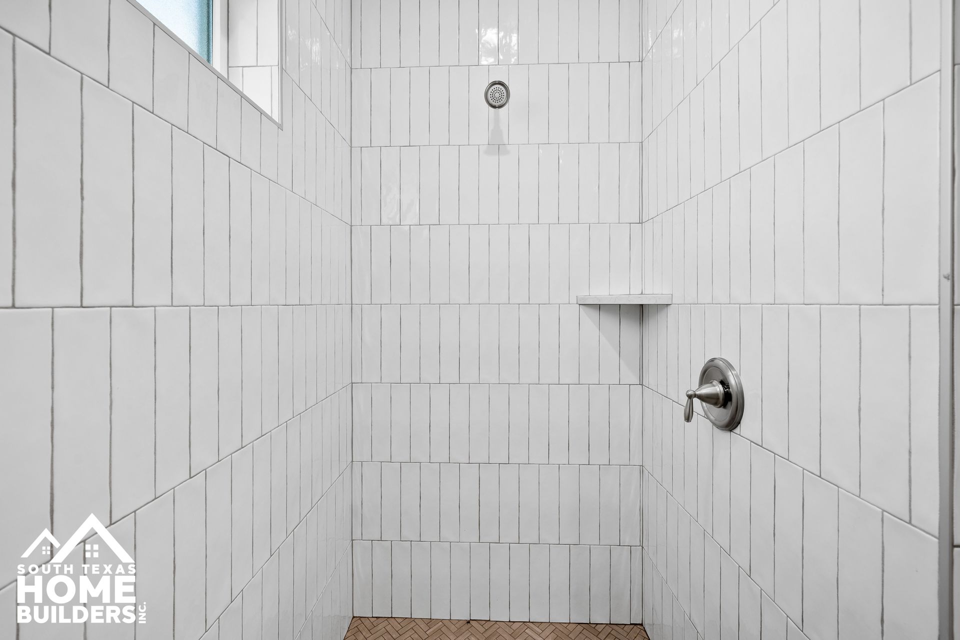 White tiled shower with a small shelf and silver faucet.