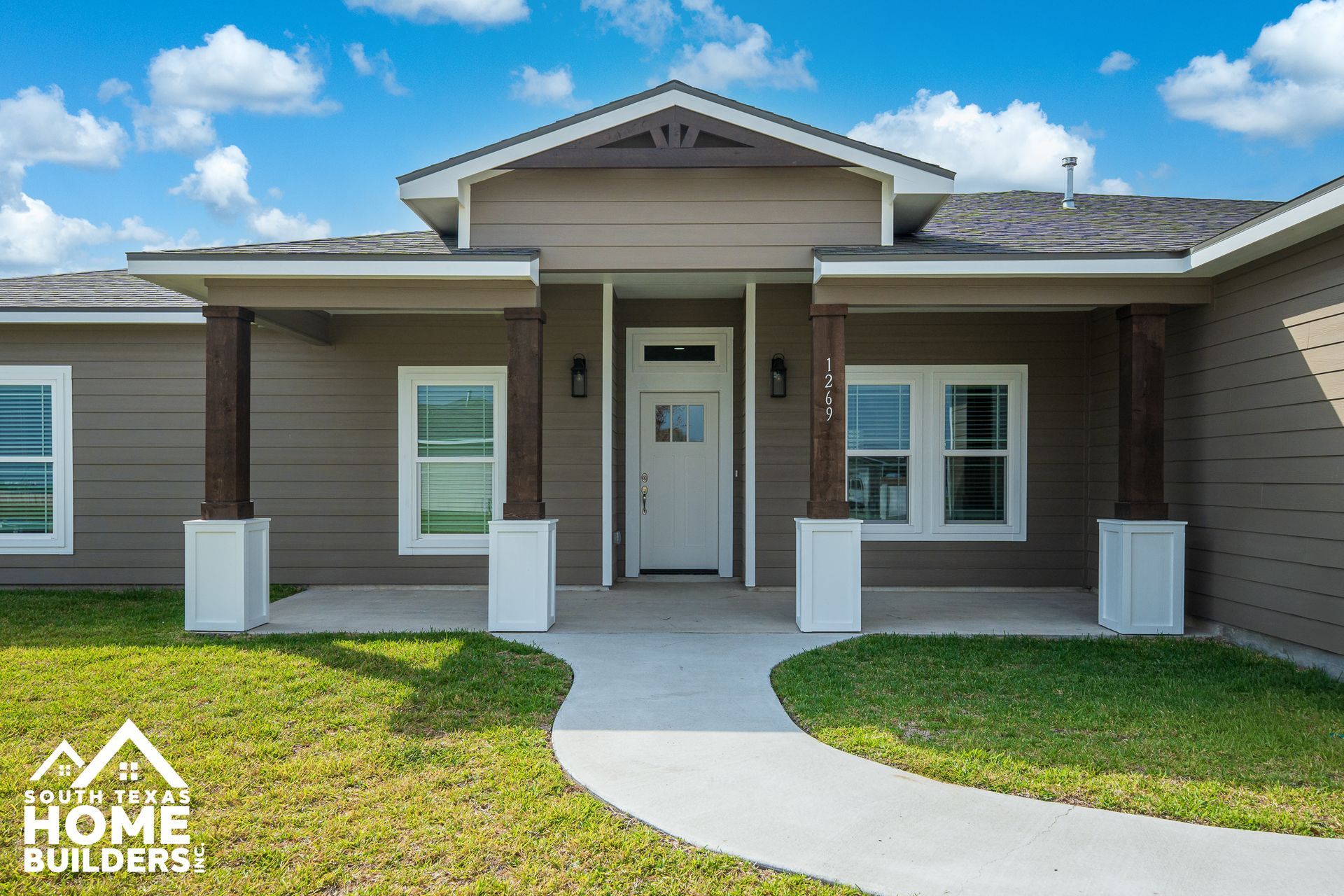 Exterior view of a modern brown house with a covered porch and walkway leading to the front door.