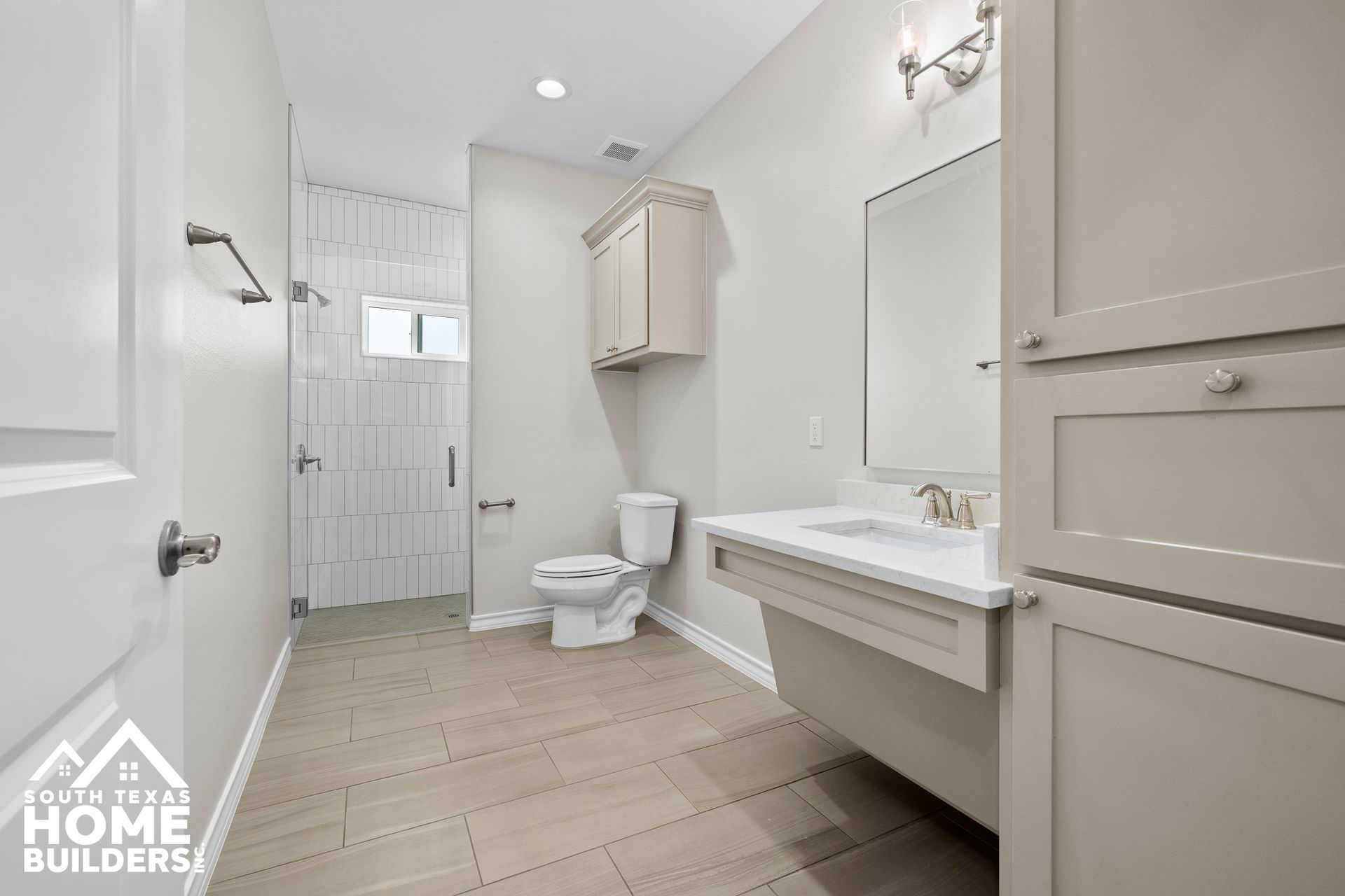 Accessible bathroom with a lowered vanity, toilet, and shower. Neutral colors, tiled floor, and a cabinet.