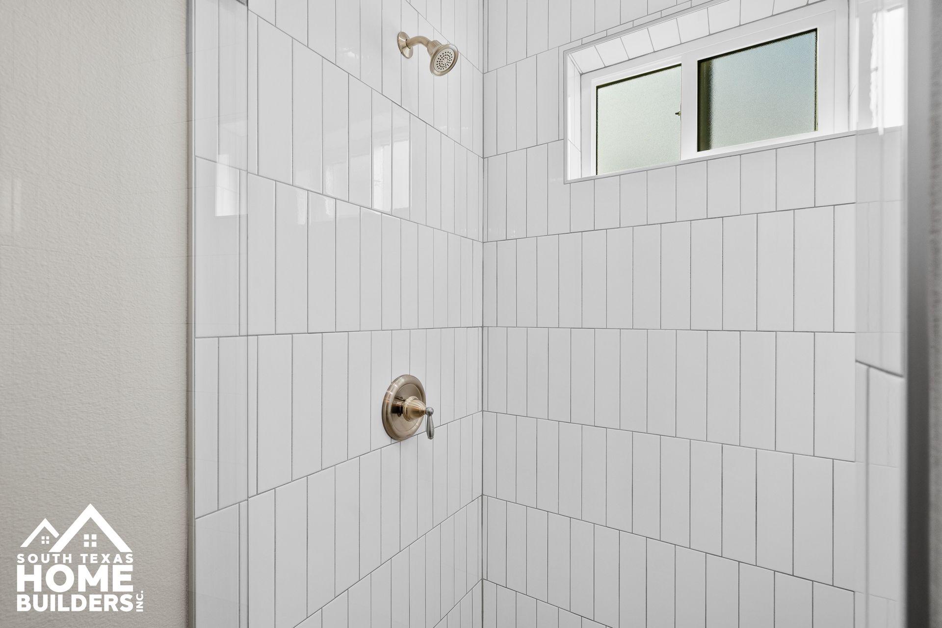 White-tiled shower with window, faucet, and showerhead in a bathroom.