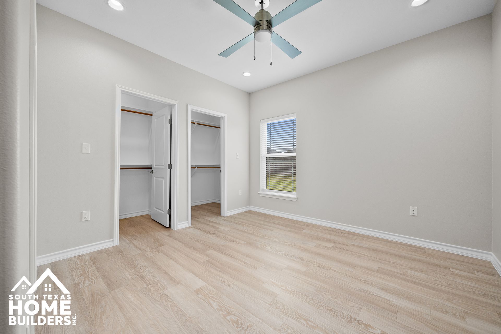 Empty bedroom with light wood flooring, two closets, and a small window.