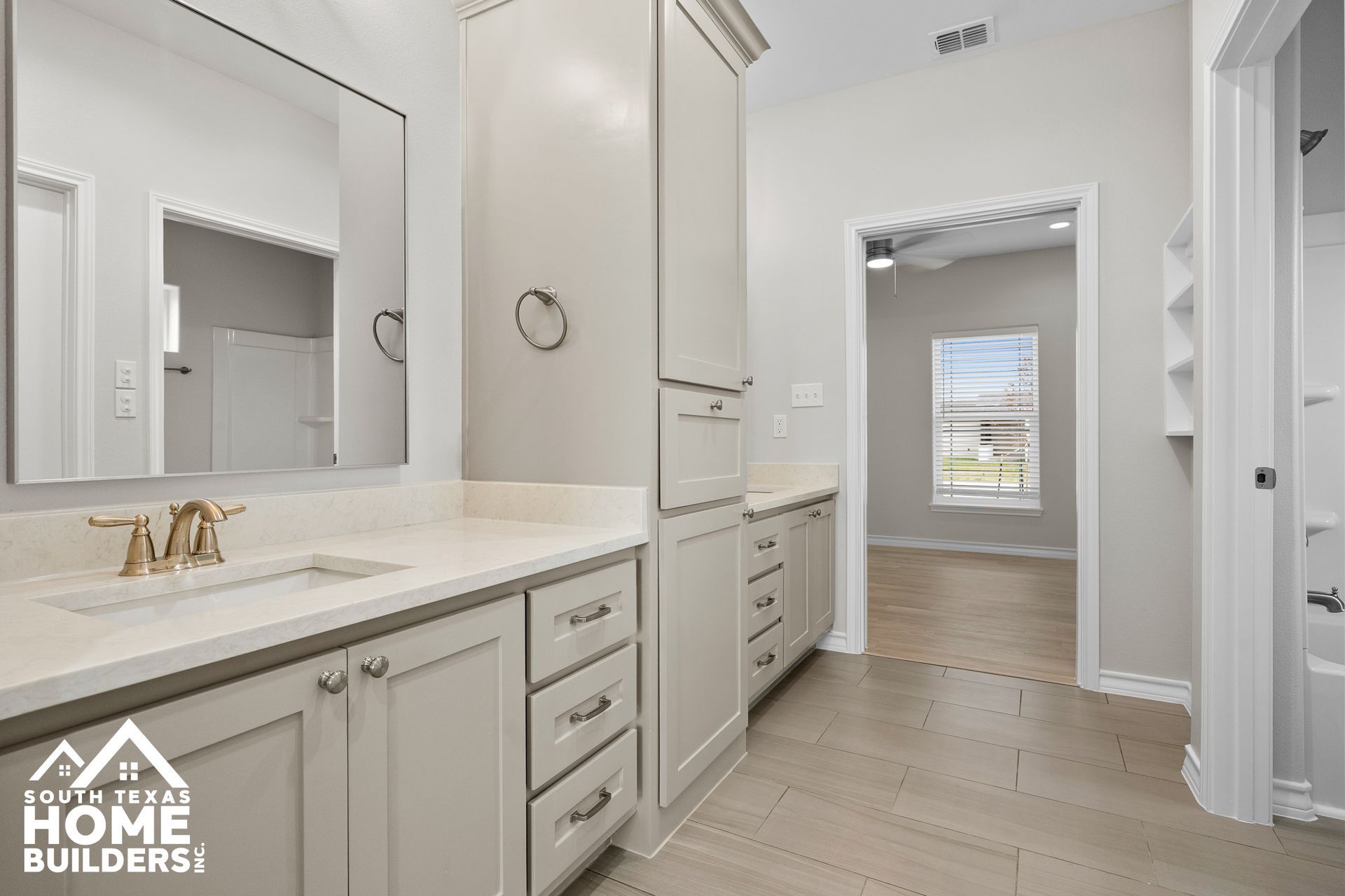 Bathroom with light gray cabinets, white countertop, and doorway to a bedroom.