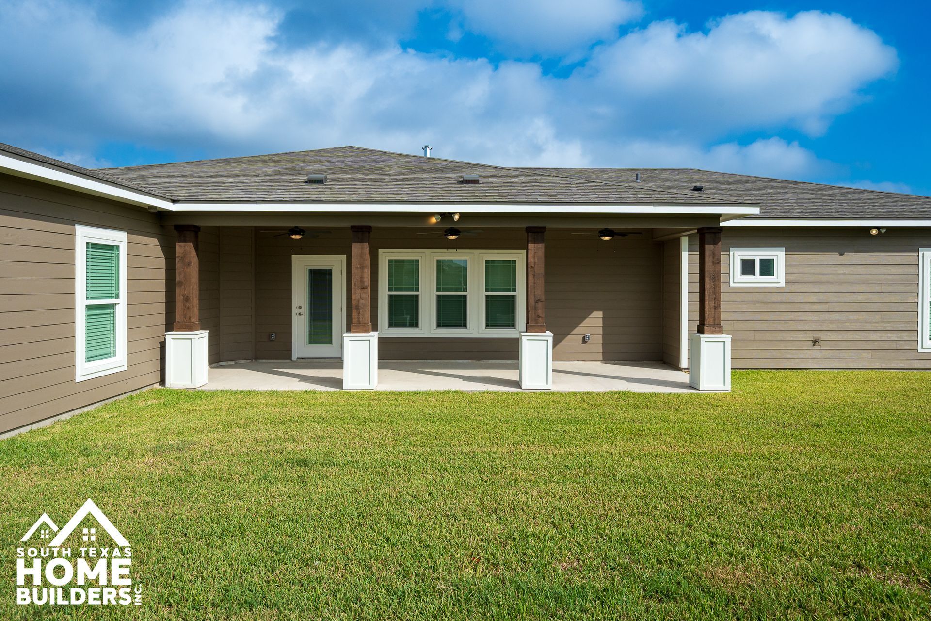 Backyard view of a house with a covered patio, brown siding, and green grass.
