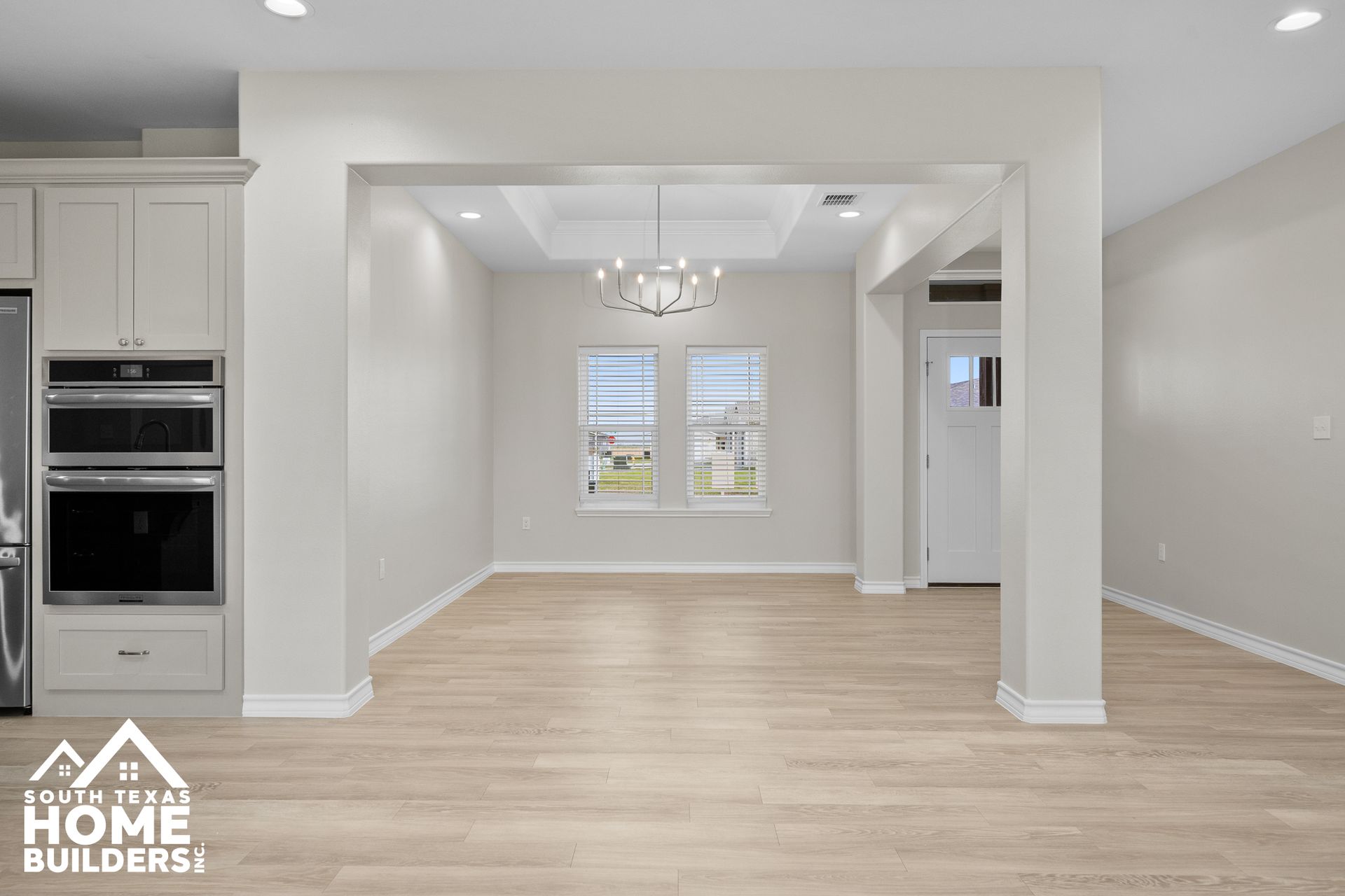 Interior view of a dining room with light wooden floors, white walls, and a chandelier.