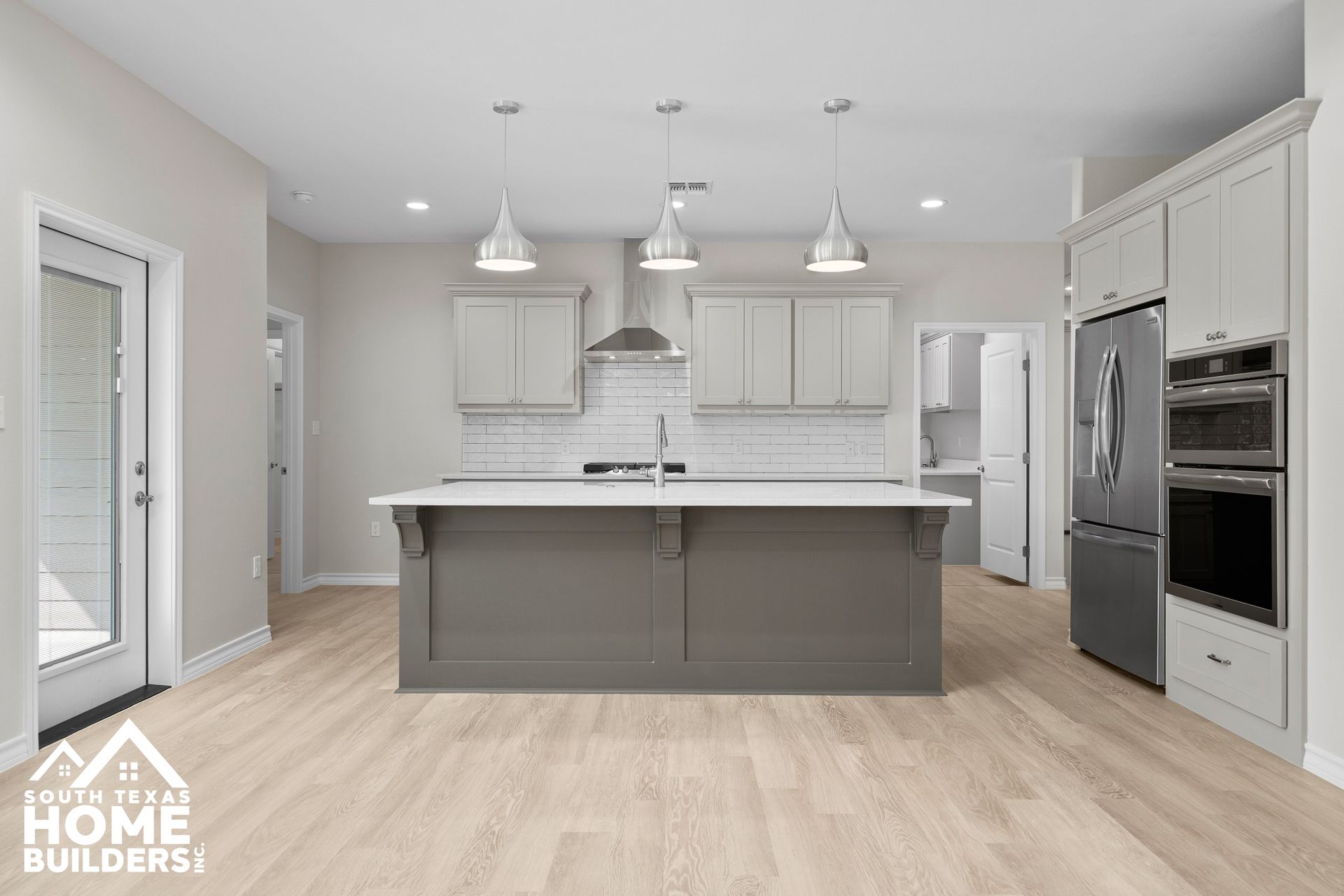 Modern kitchen with gray island, white cabinets, stainless steel appliances, and wood-look flooring.