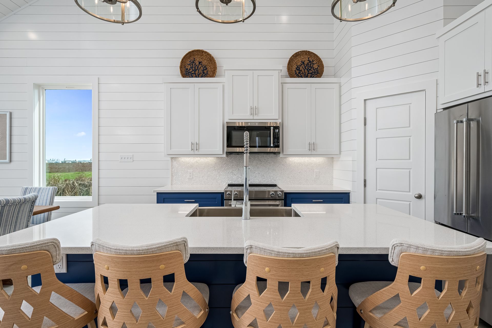 A kitchen with white cabinets , a large island , a sink , a microwave , and a refrigerator.
