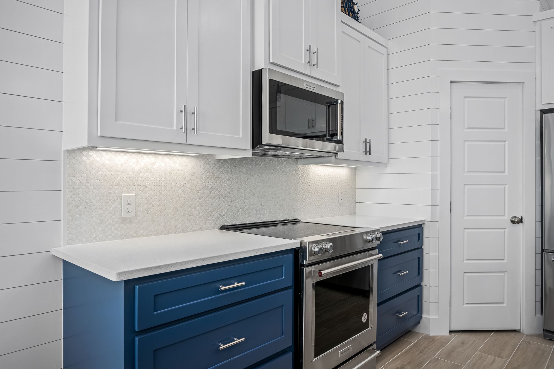 A kitchen with blue cabinets , white cabinets , stainless steel appliances and a microwave.
