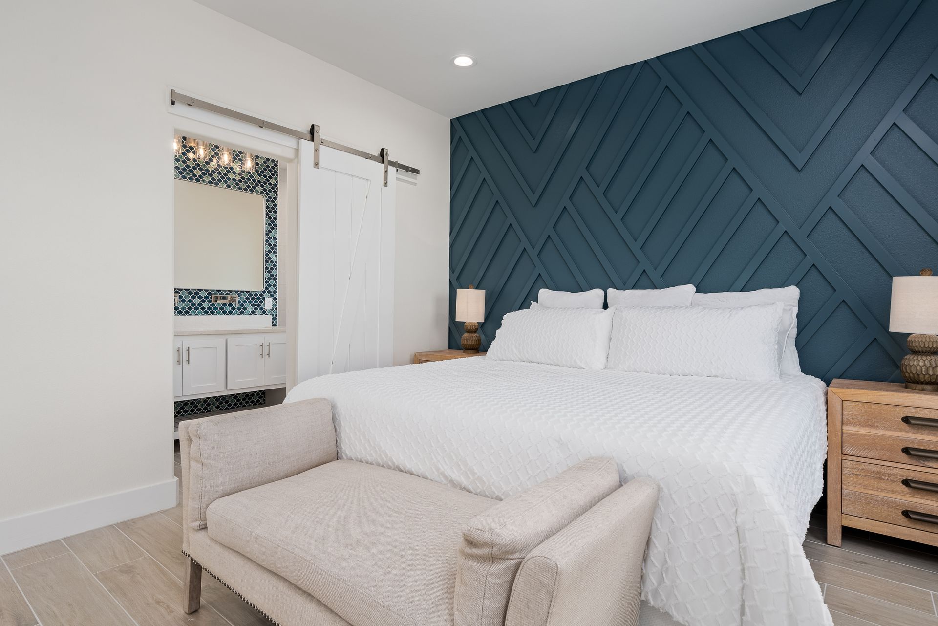 A bedroom with a bed , chair , nightstand , mirror and blue wall.