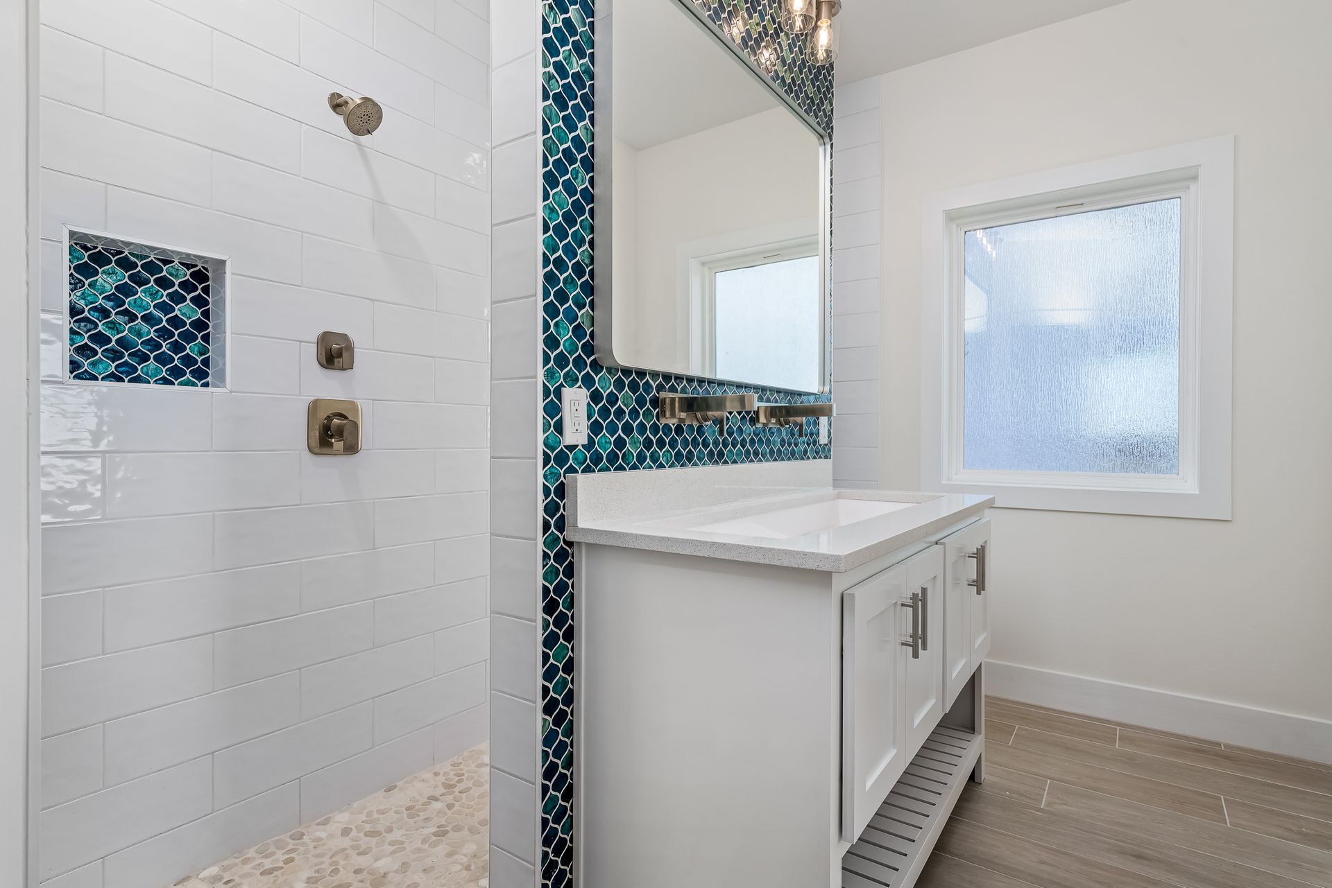 A bathroom with a walk in shower , sink , mirror and window.