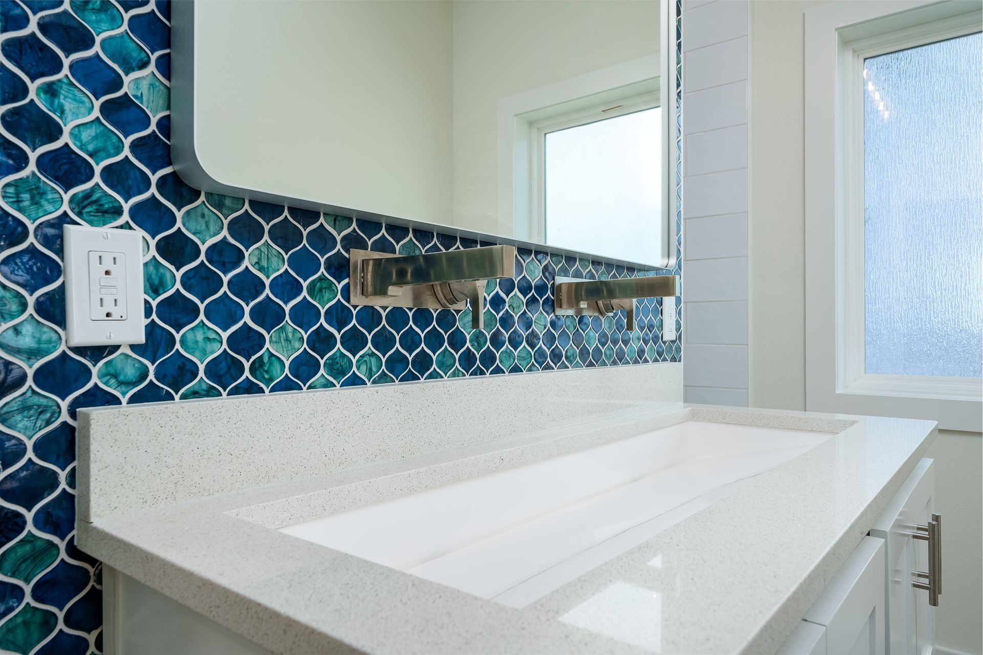 A bathroom with a sink , mirror and blue tiles.