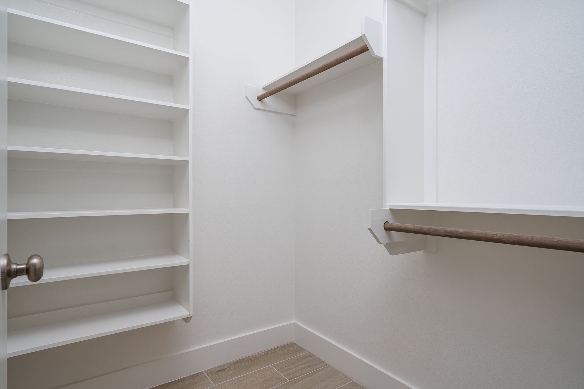 An empty walk in closet with white shelves and a door.