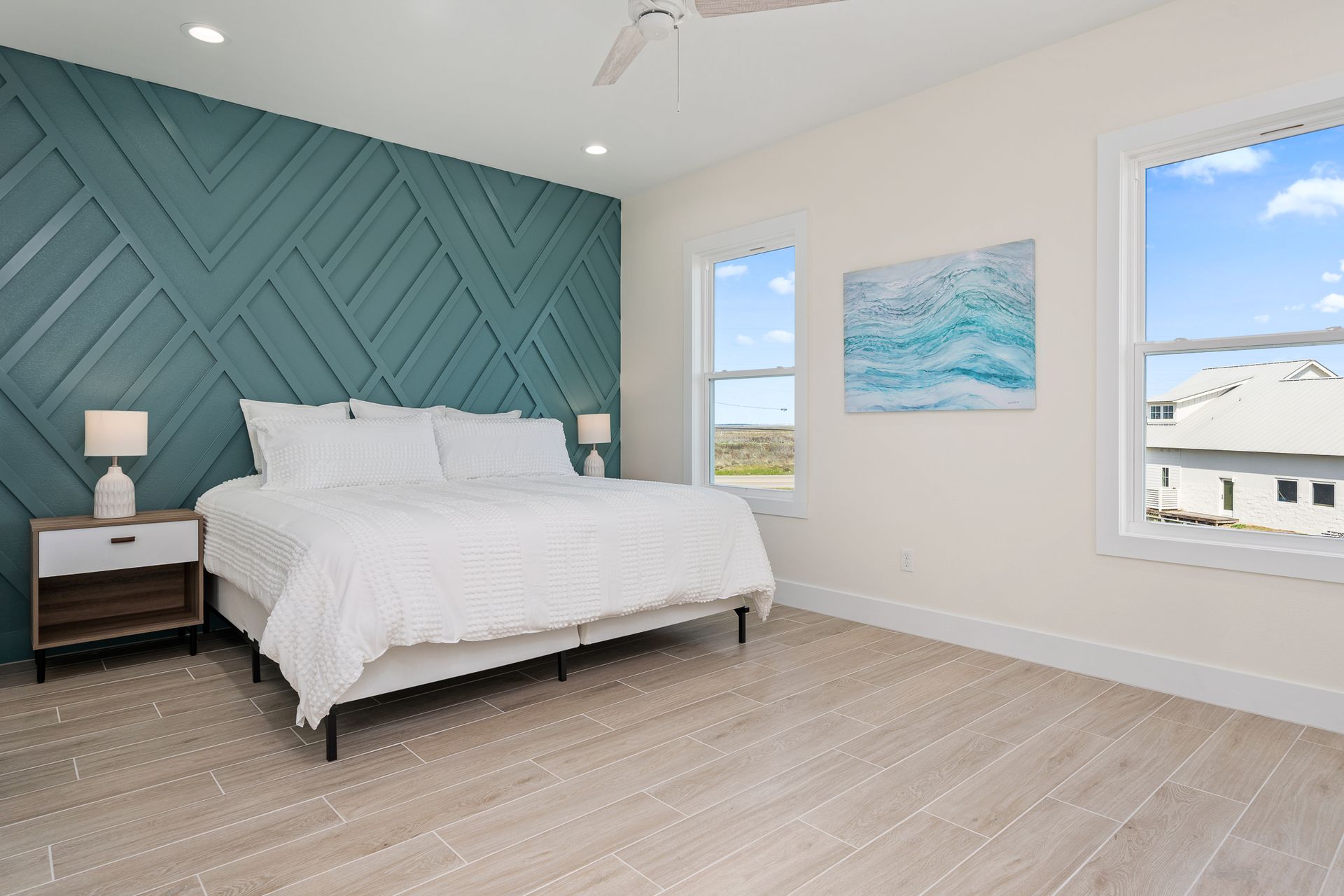 A bedroom with a large bed , two windows and a ceiling fan.
