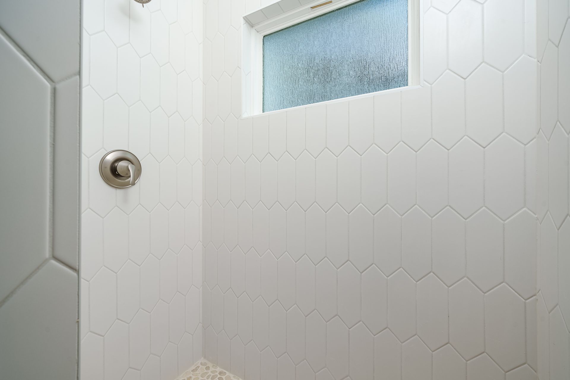 A shower with white tiles and a window.