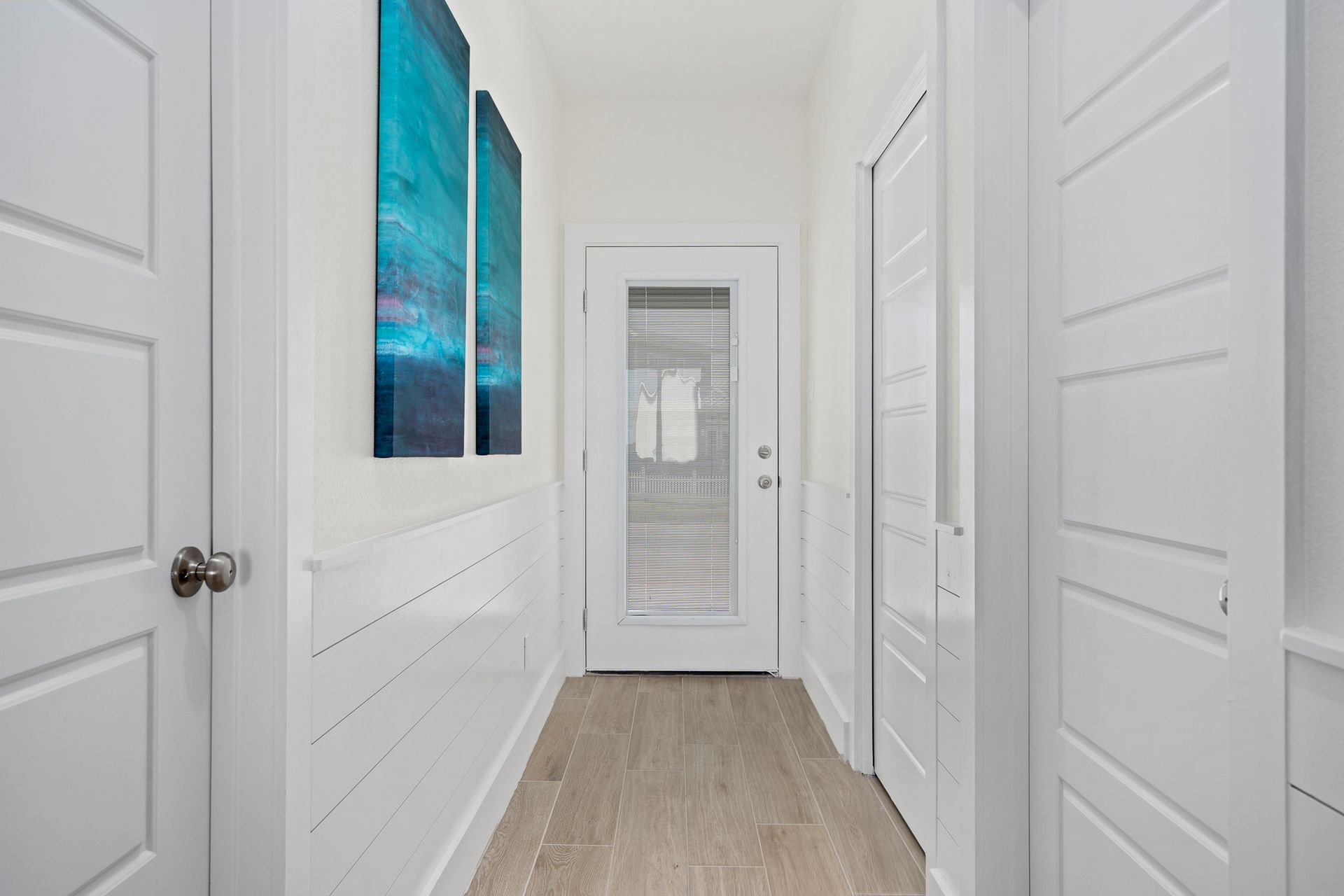 A hallway in a house with white doors and paintings on the wall.