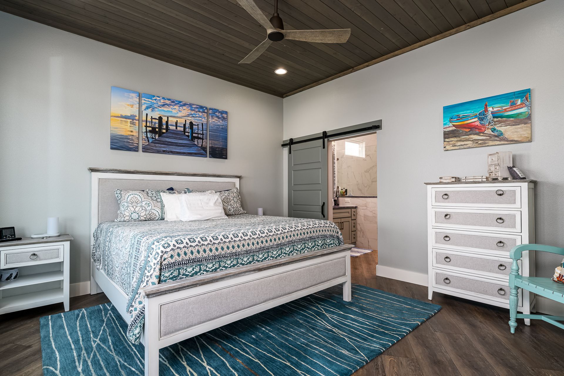 A bedroom with a bed , dresser , nightstand , rug and ceiling fan.