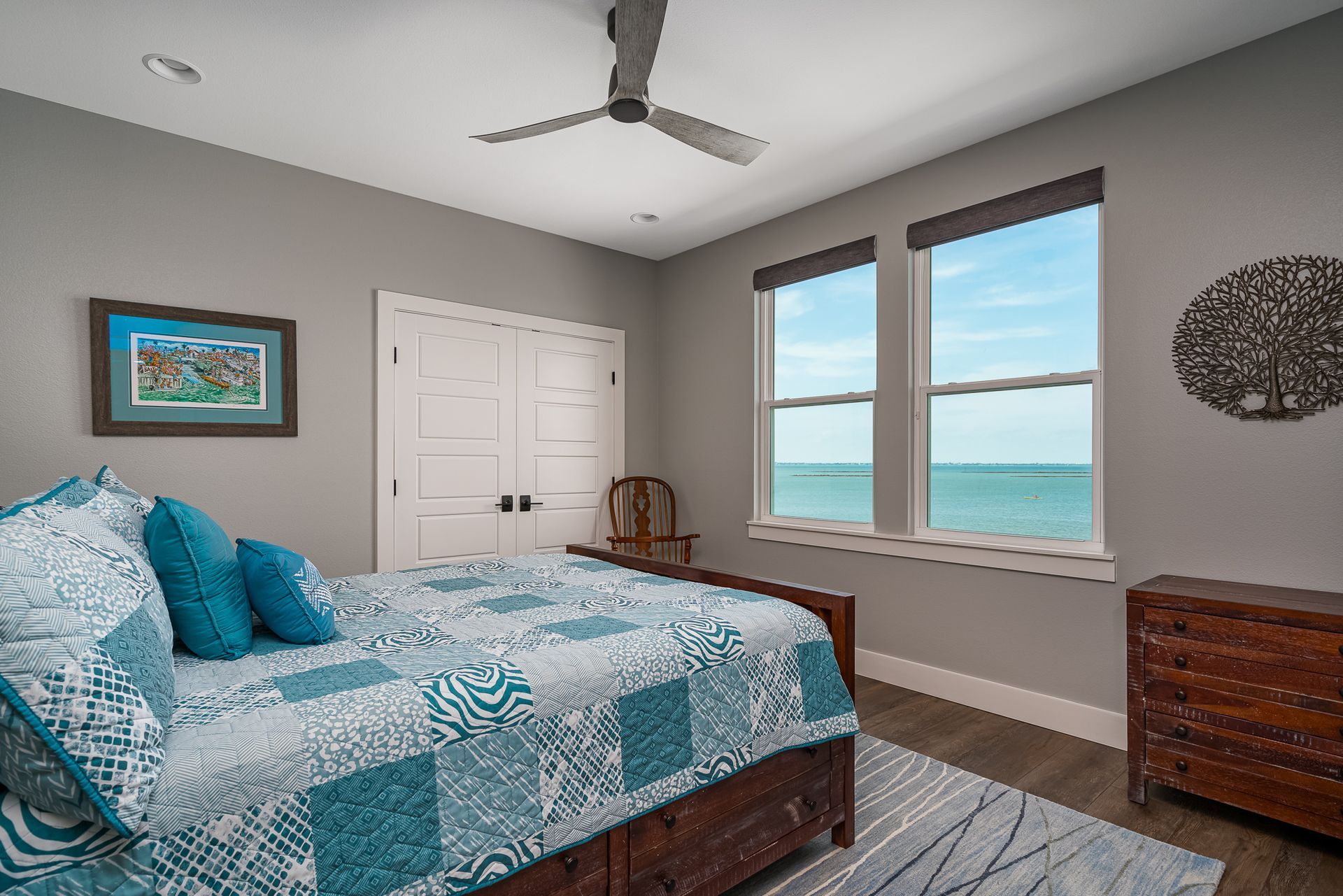 A bedroom with a bed , dresser , and ceiling fan with a view of the ocean.