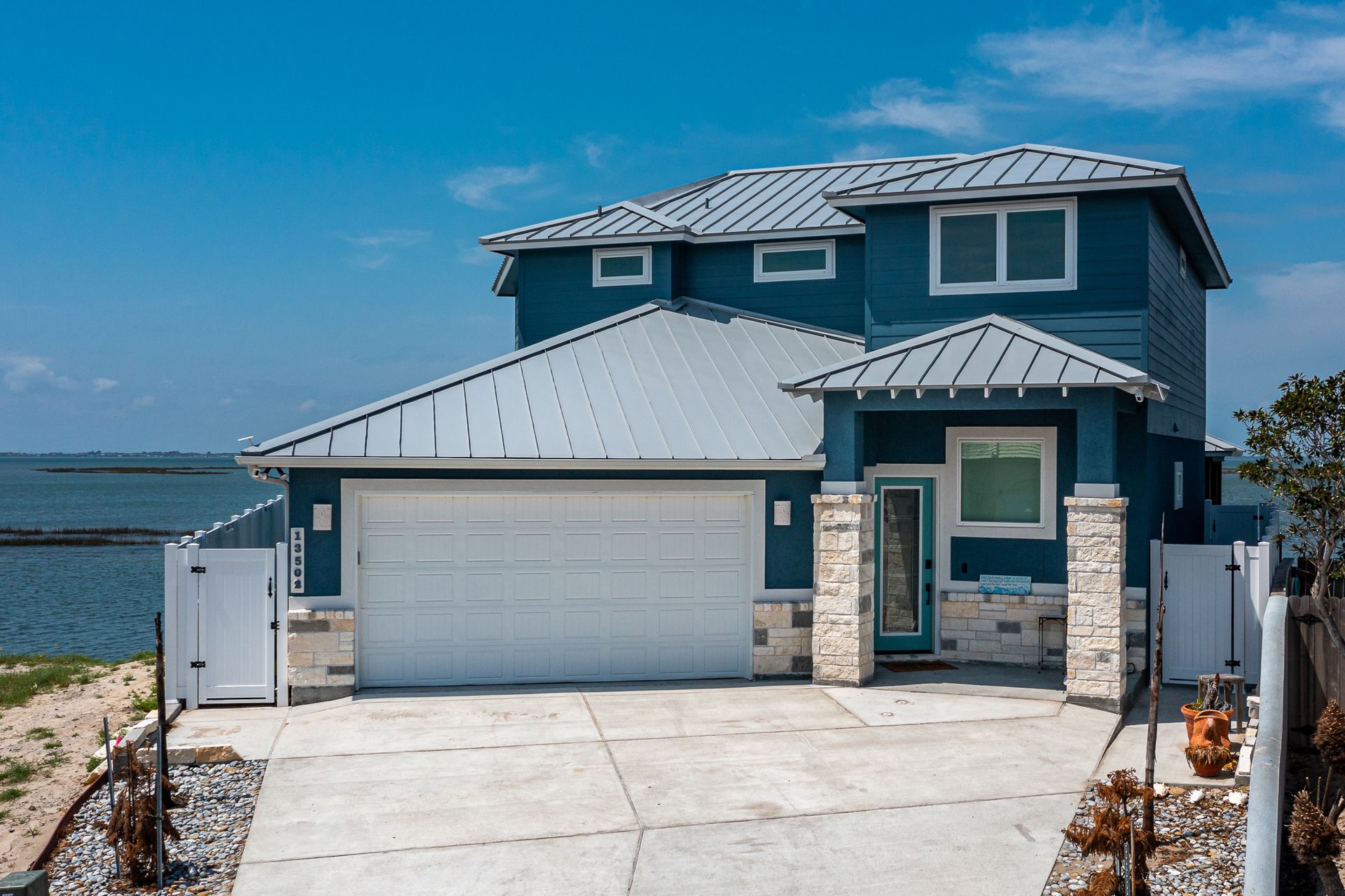 A blue house with a white garage door is next to a body of water