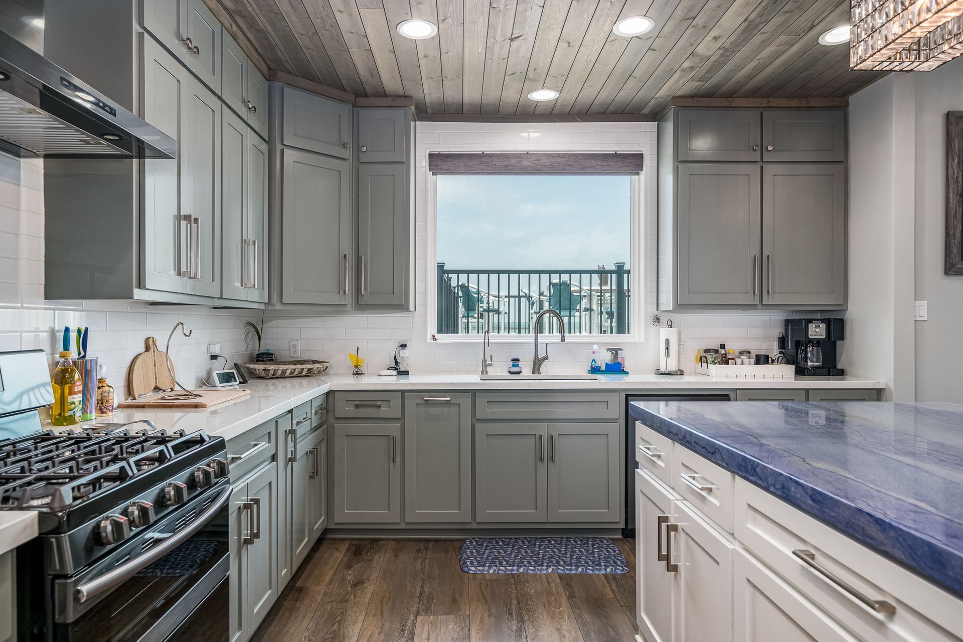 A kitchen with gray cabinets , a stove , a sink , and a window.