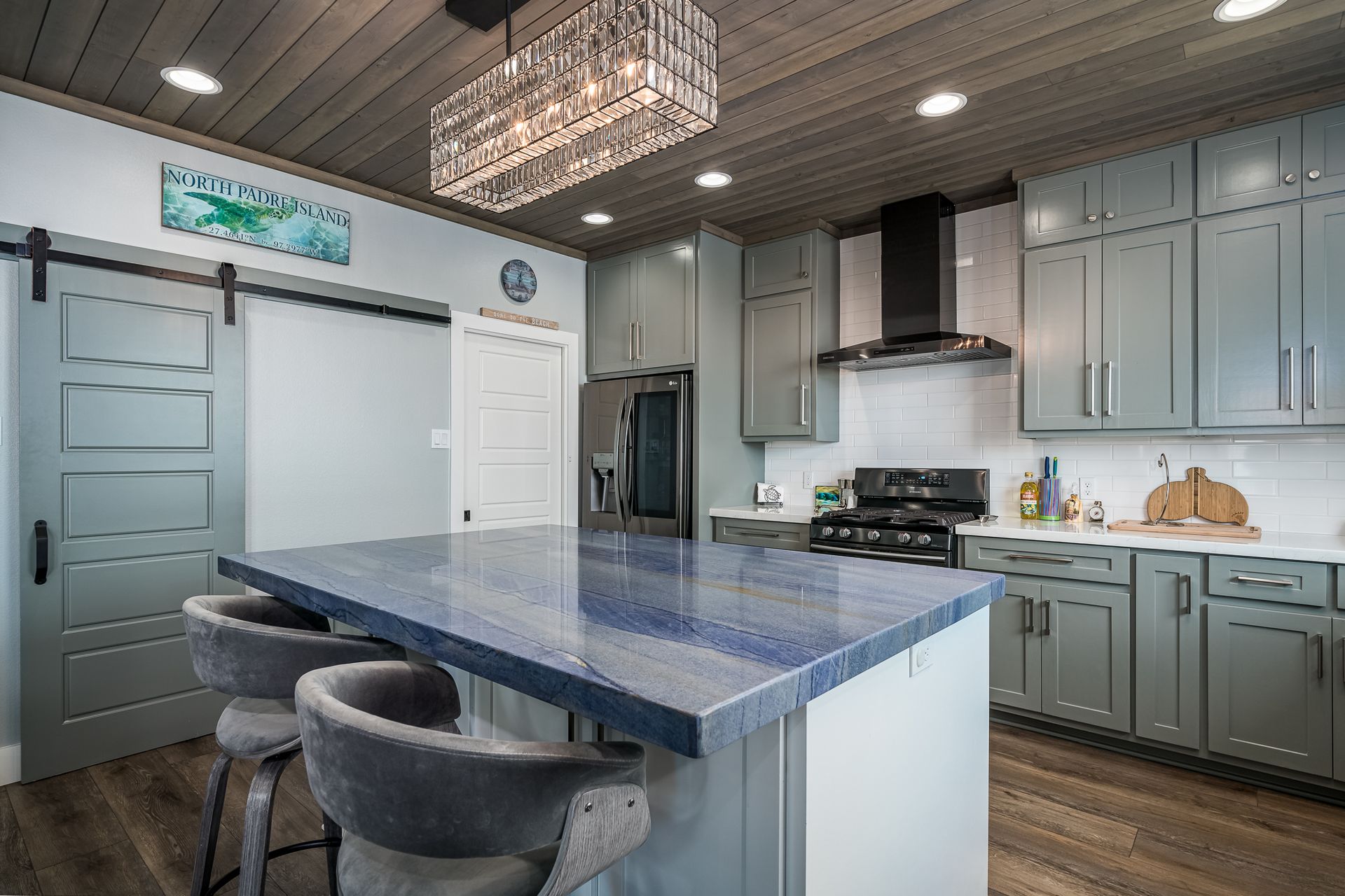 A kitchen with a large island and stools and a chandelier hanging from the ceiling.