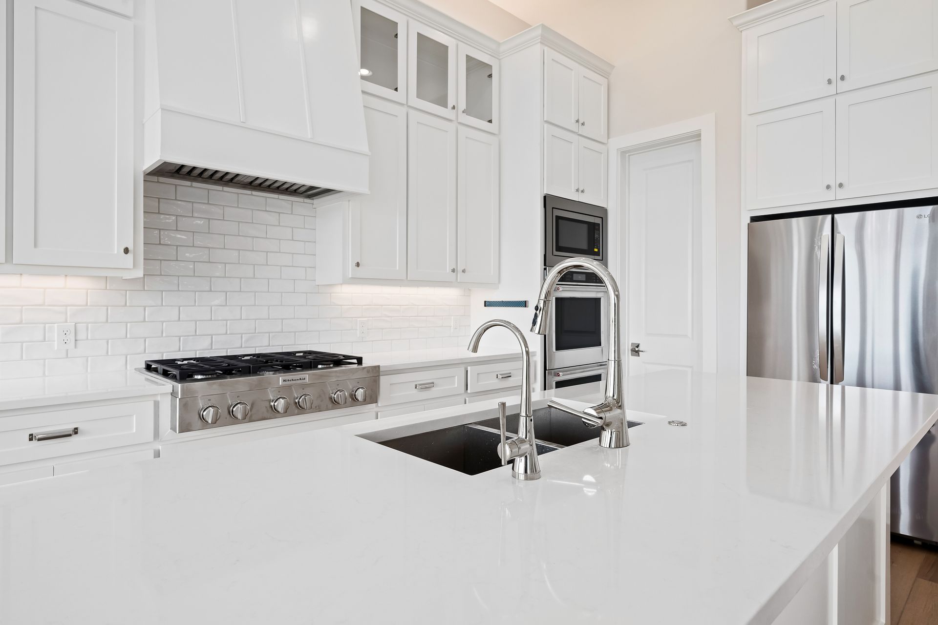 A kitchen with white cabinets , a sink , a stove , and a refrigerator.