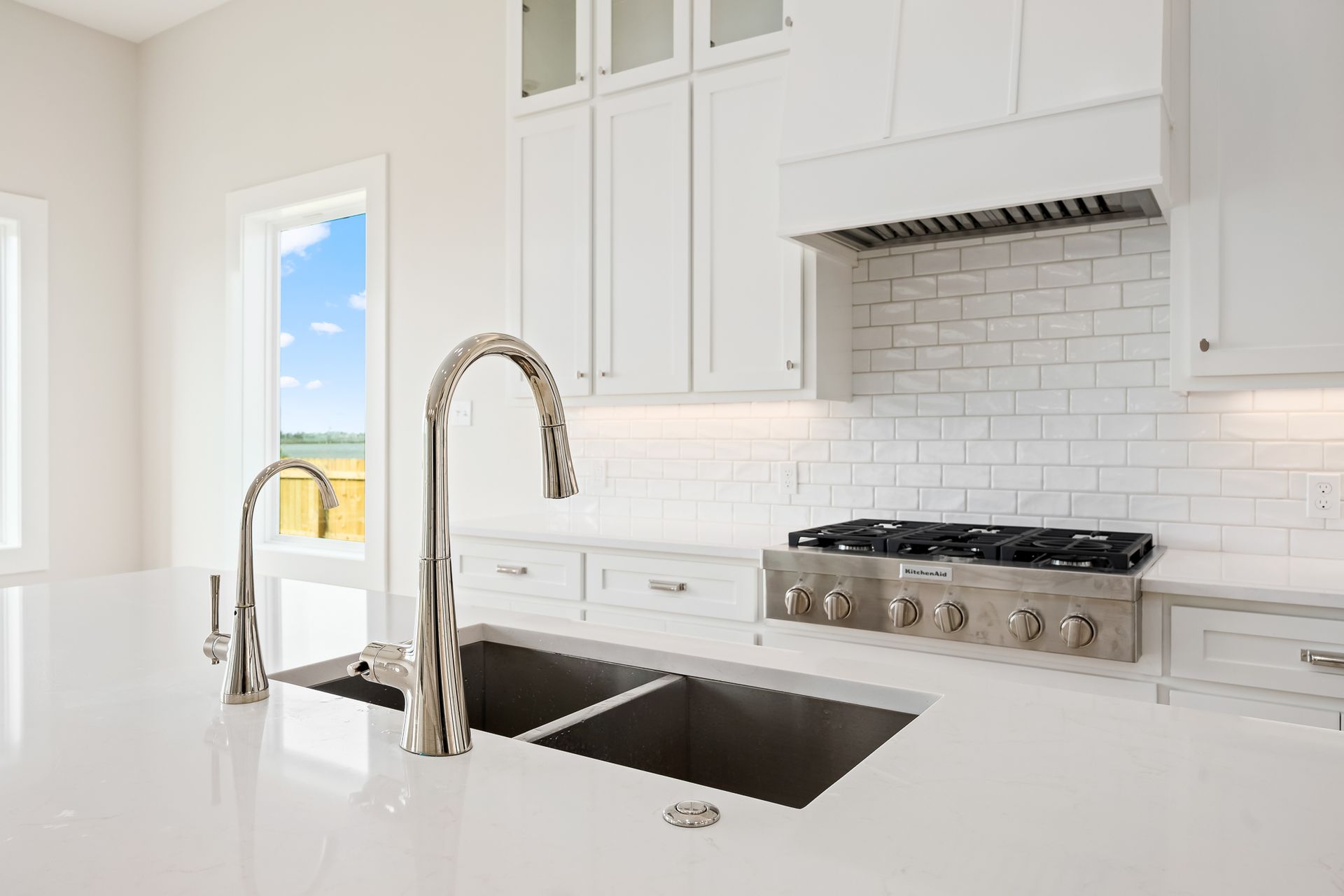 A kitchen with white cabinets , a stove , a sink , and a window.