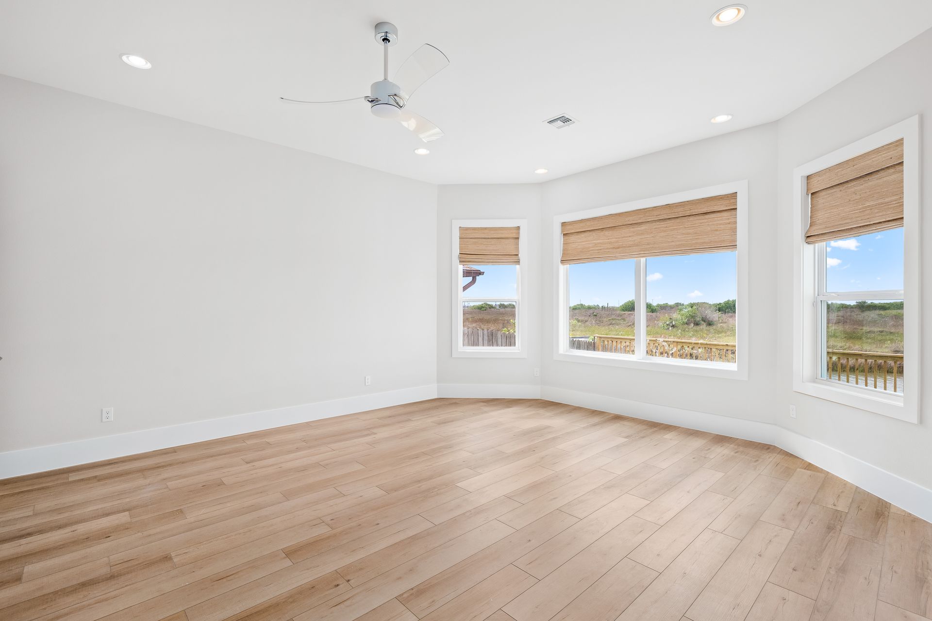 A large empty room with hardwood floors and a ceiling fan.