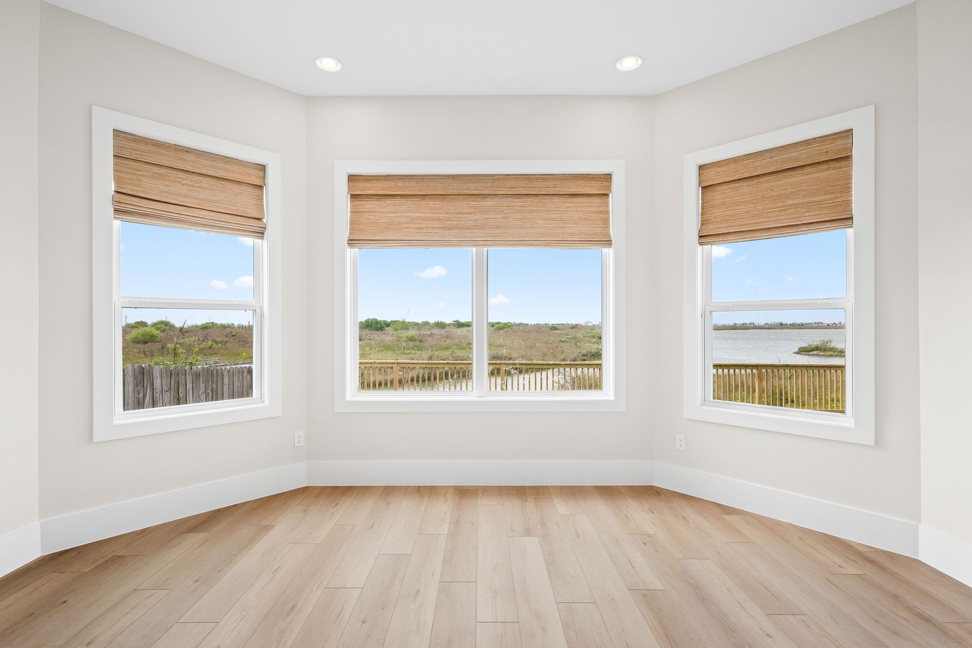 An empty room with three windows and wooden floors.