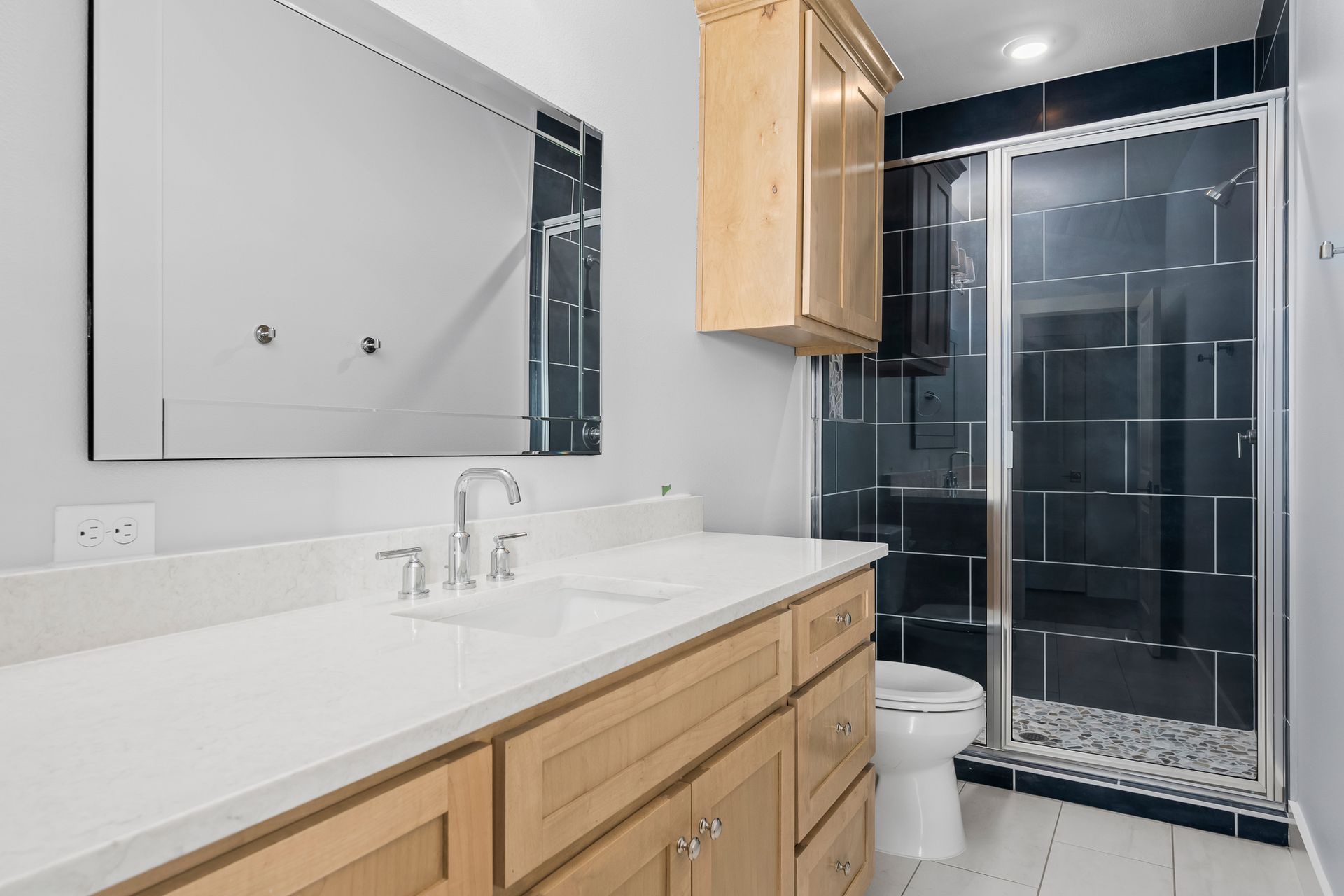 A bathroom with a toilet , sink , mirror and walk in shower.