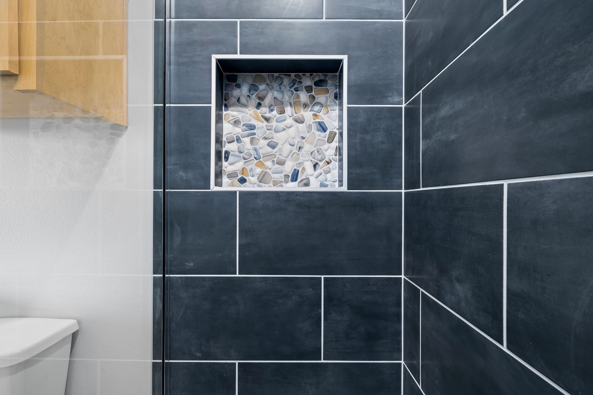 A bathroom with black tiles , a toilet , and a shower stall.