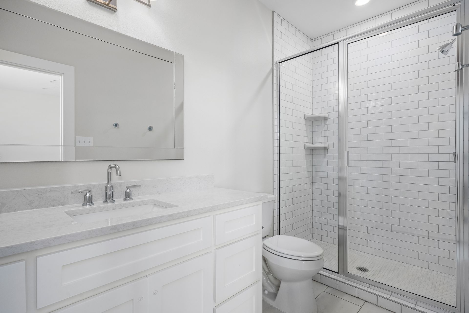 A bathroom with a toilet , sink , mirror and shower stall.