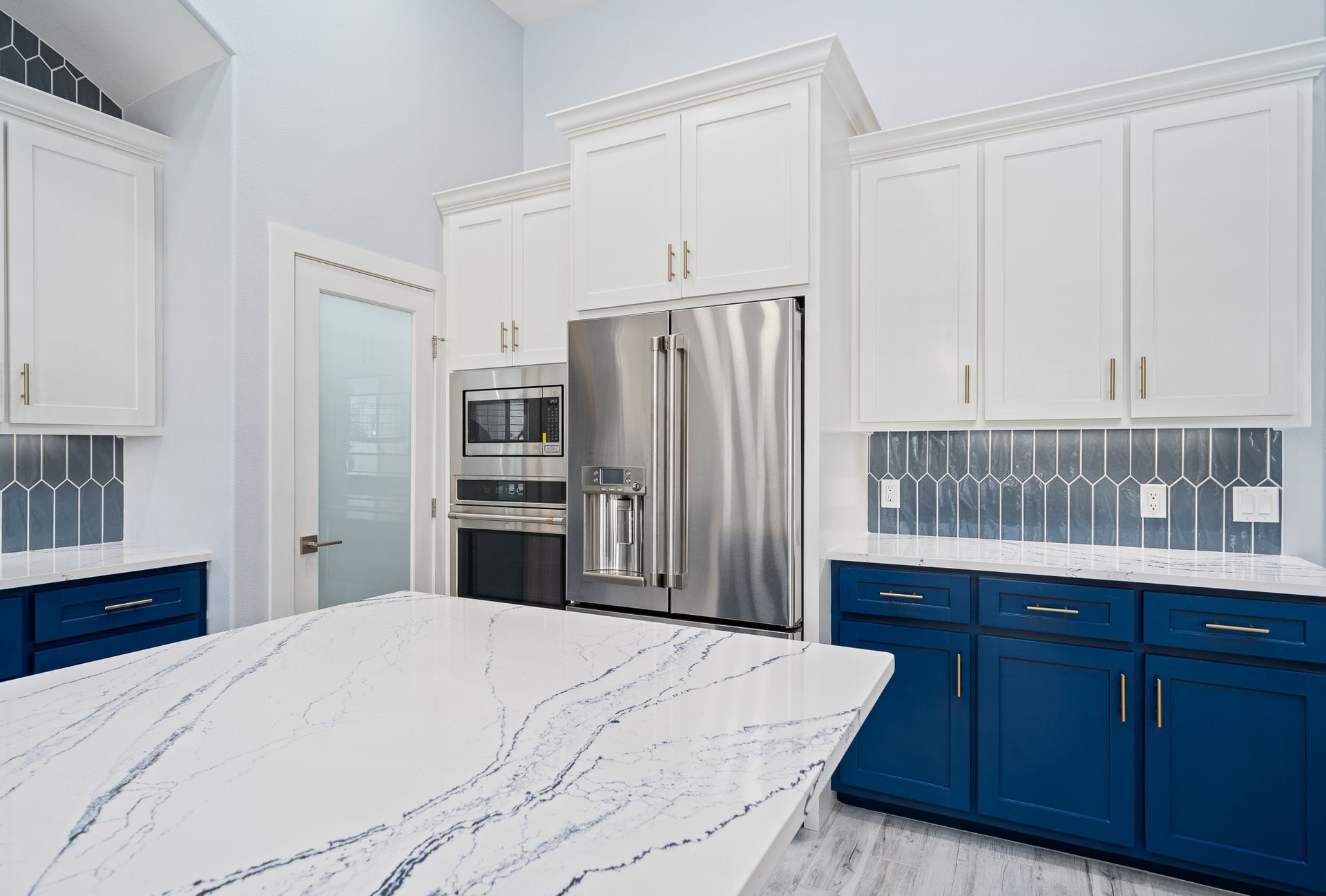 A kitchen with blue cabinets , white cabinets , stainless steel appliances , and a large island.