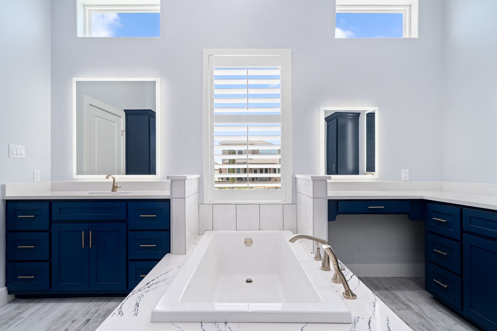 A bathroom with a bathtub , sinks , mirrors and blue cabinets.