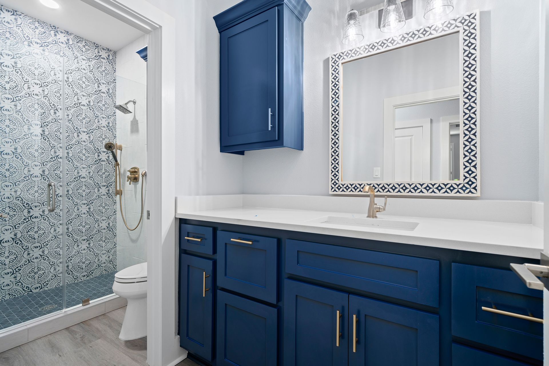 A bathroom with blue cabinets , a sink , a mirror and a toilet.