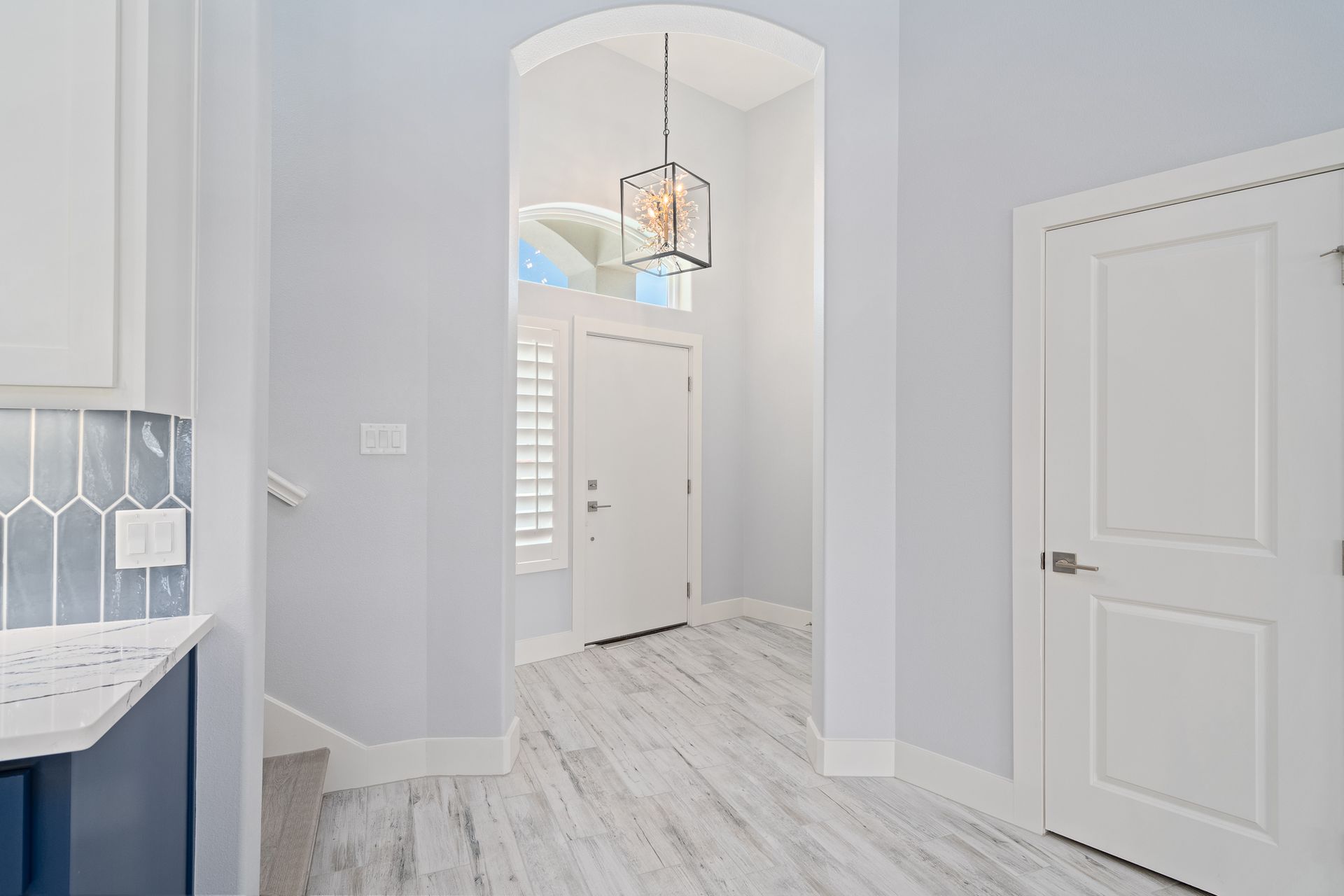 A hallway in a house with white walls and white doors leading to the front door.