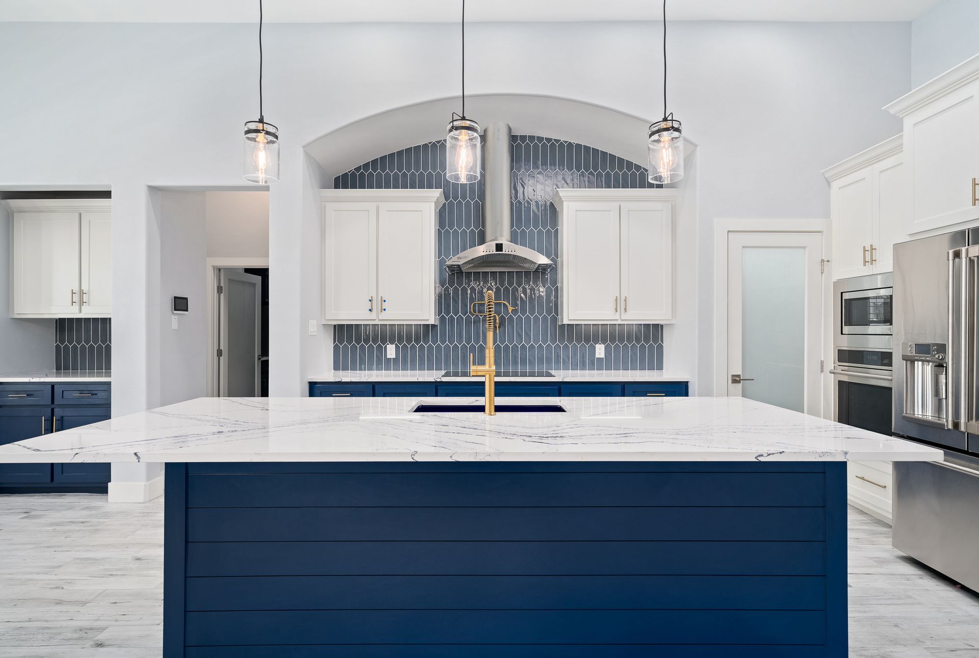 A kitchen with a blue island , white cabinets , stainless steel appliances , and a sink.