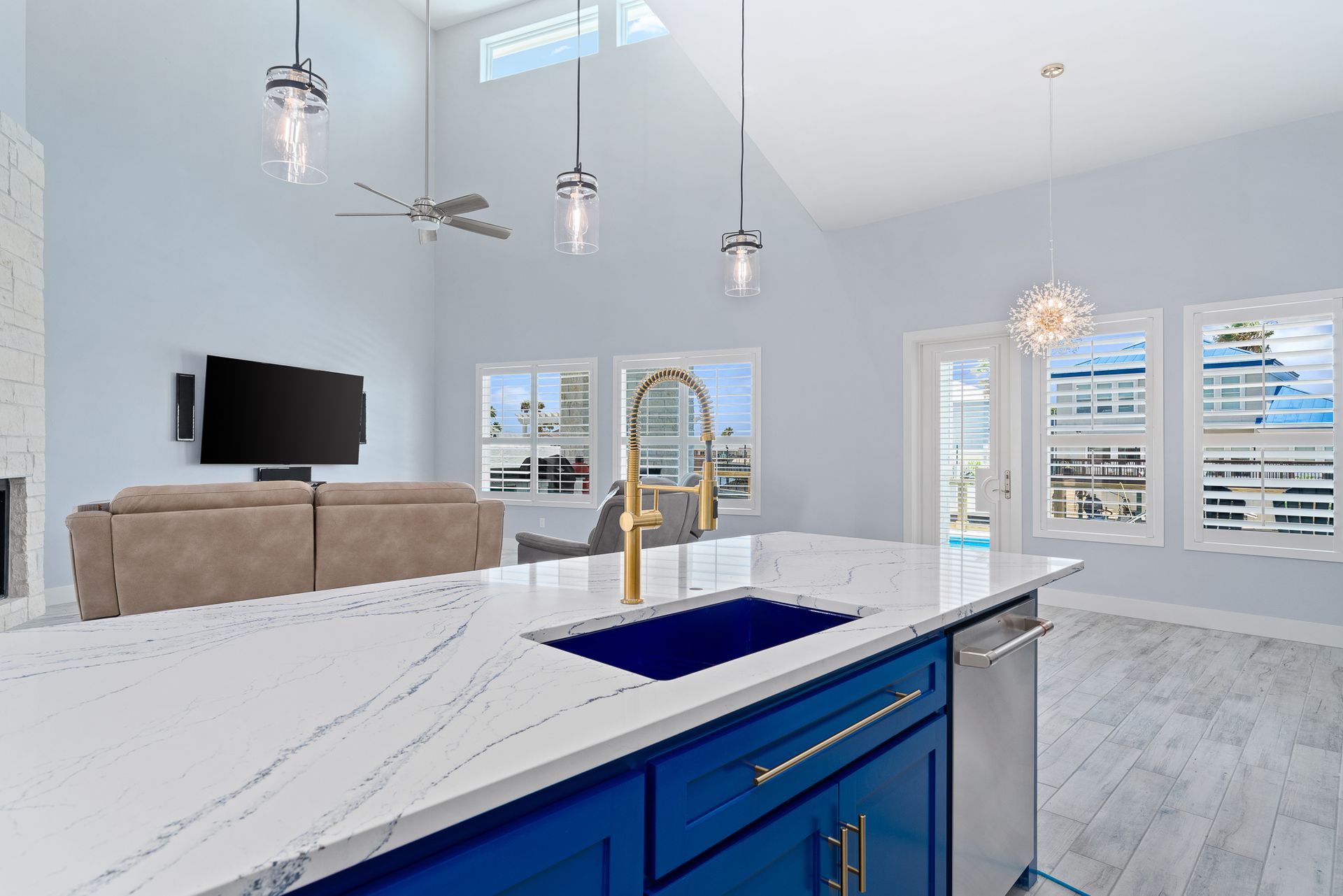 A kitchen with blue cabinets , white counter tops , a sink and a television.