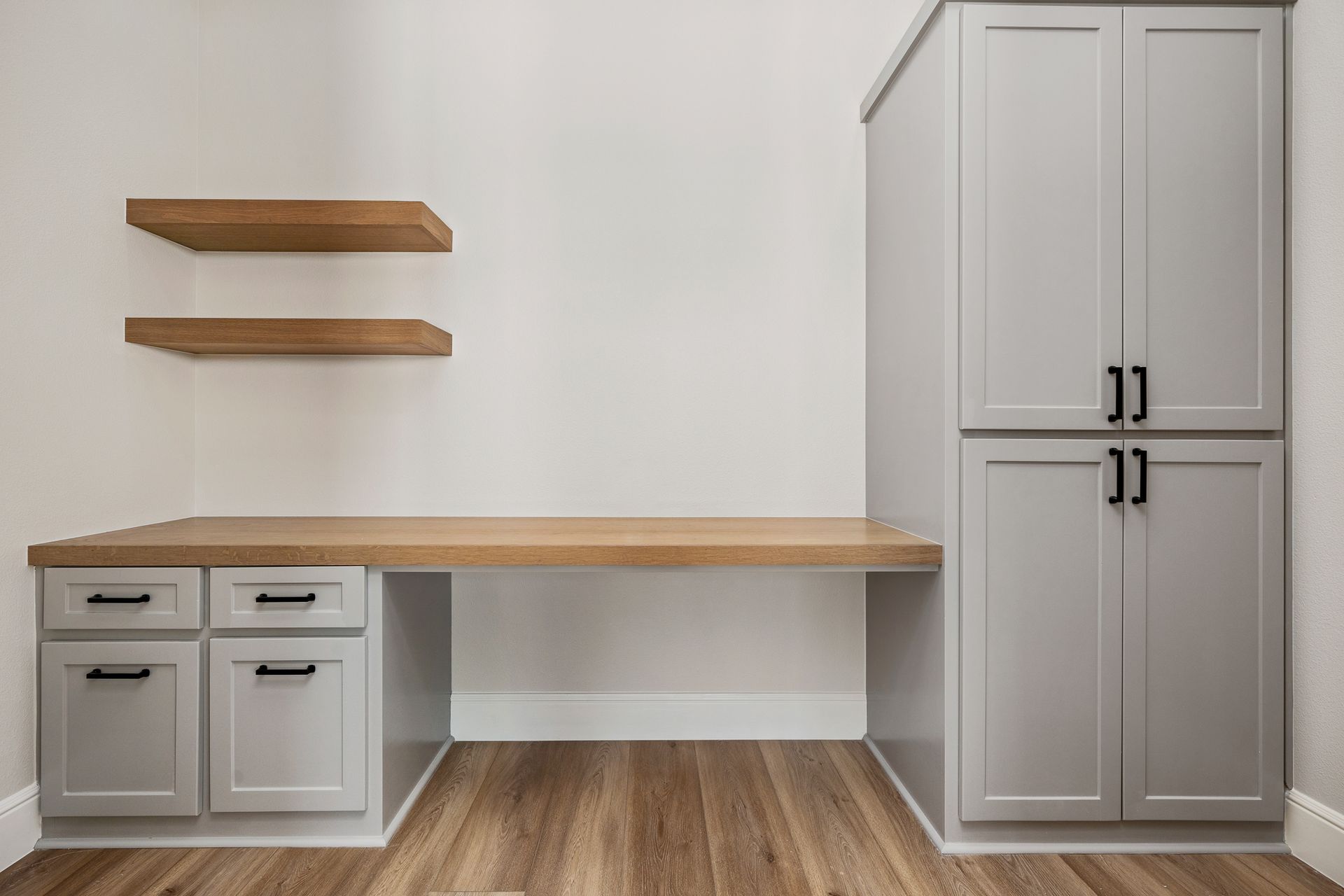 A room with a desk , cabinets , shelves and a wooden floor.