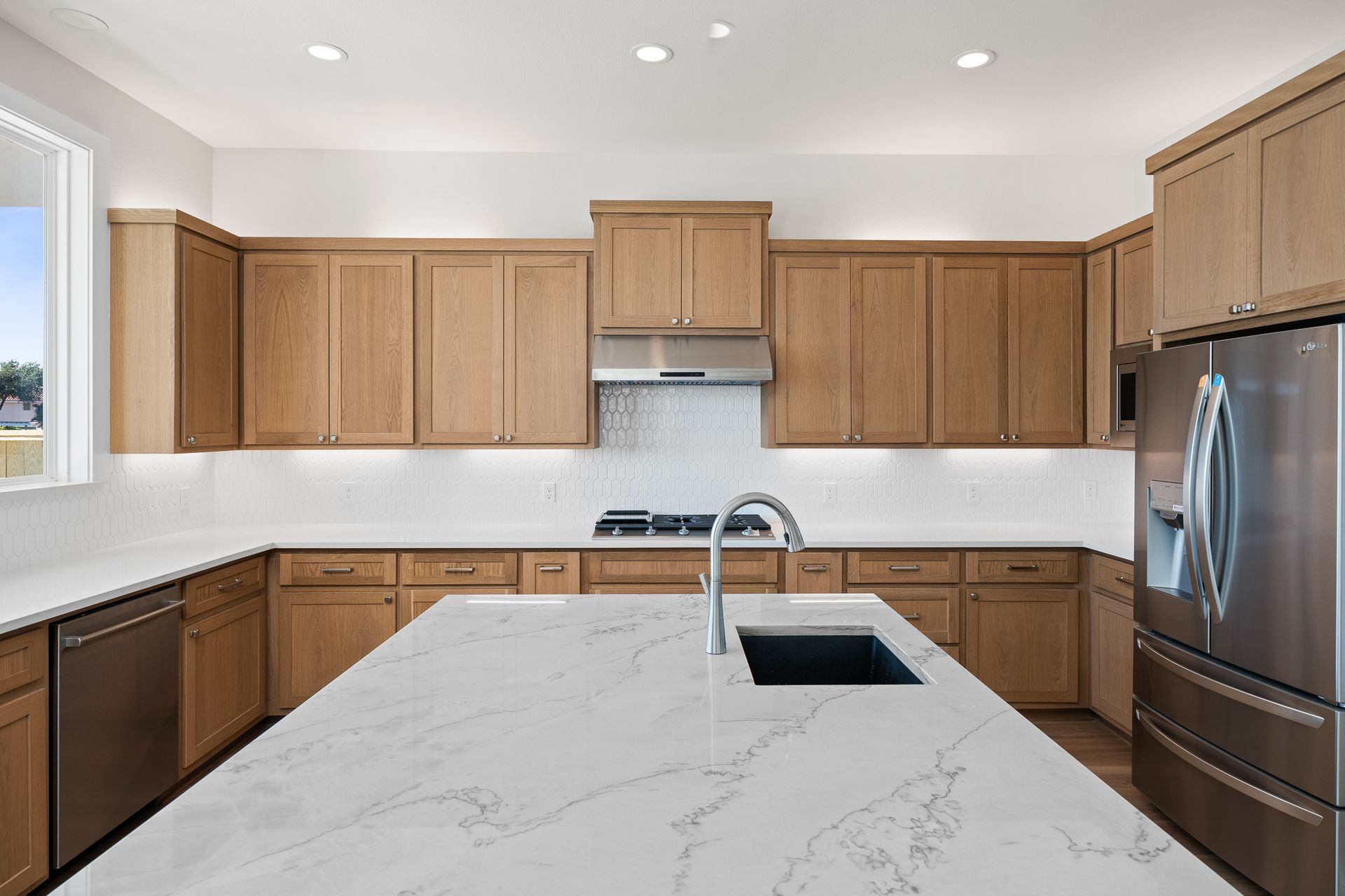 A kitchen with wooden cabinets , white counter tops , stainless steel appliances and a large island.