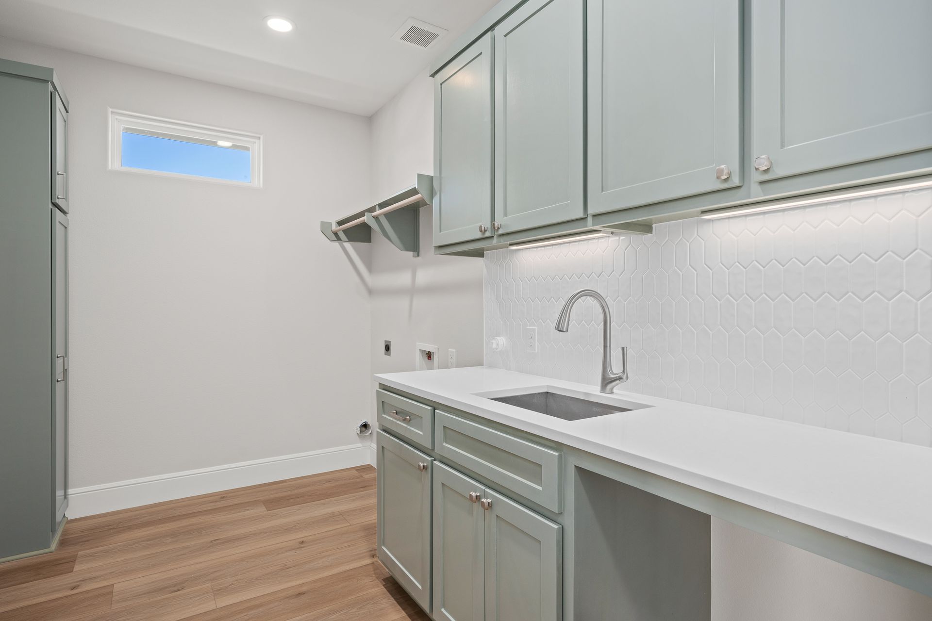 A laundry room with a sink , cabinets , and hardwood floors.